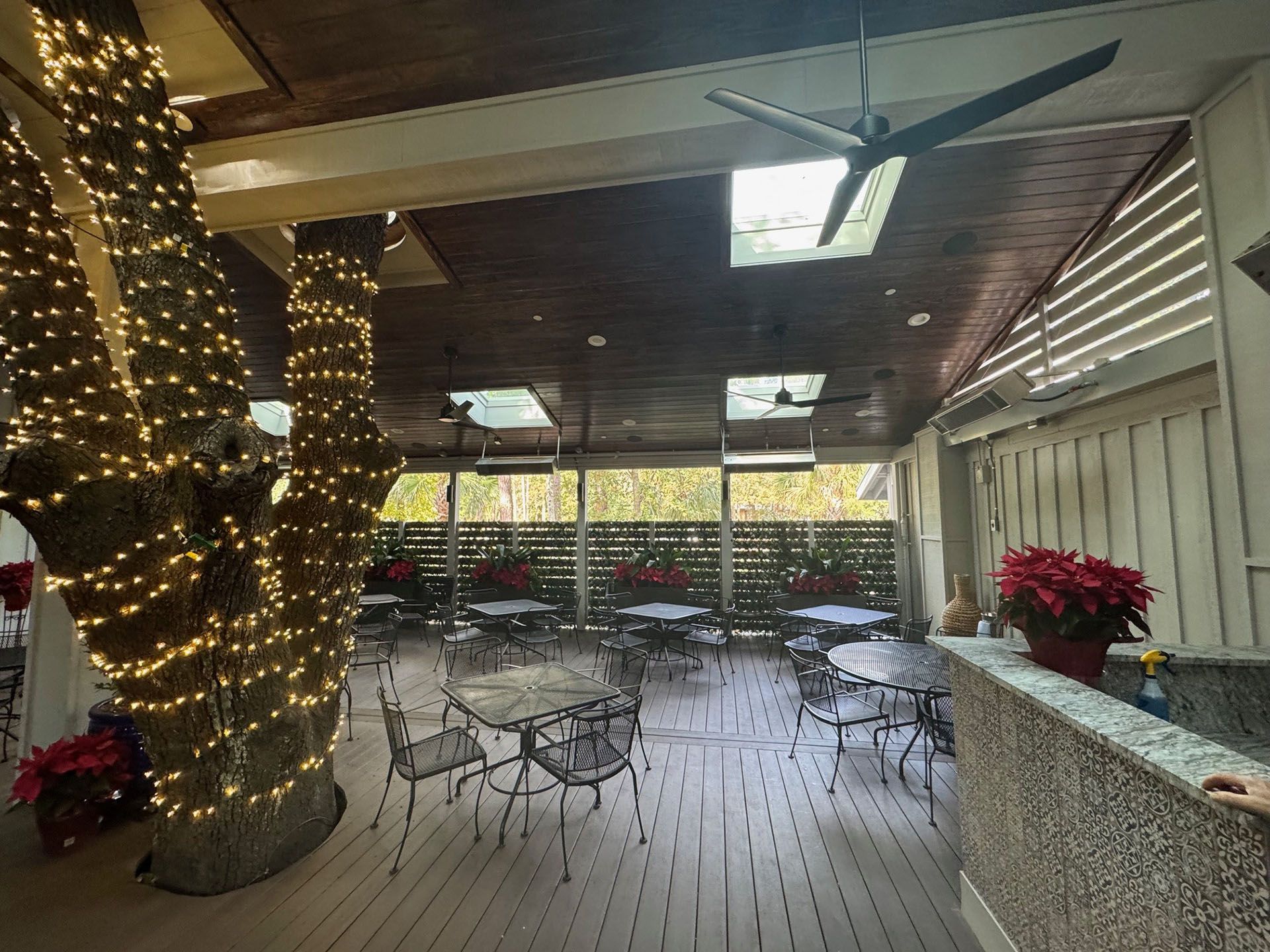 Commercial restaurant remodel and expansion  - Nunzios/After: Outdoor dining area with tables and chairs under a wood ceiling, with trees wrapped in lights.