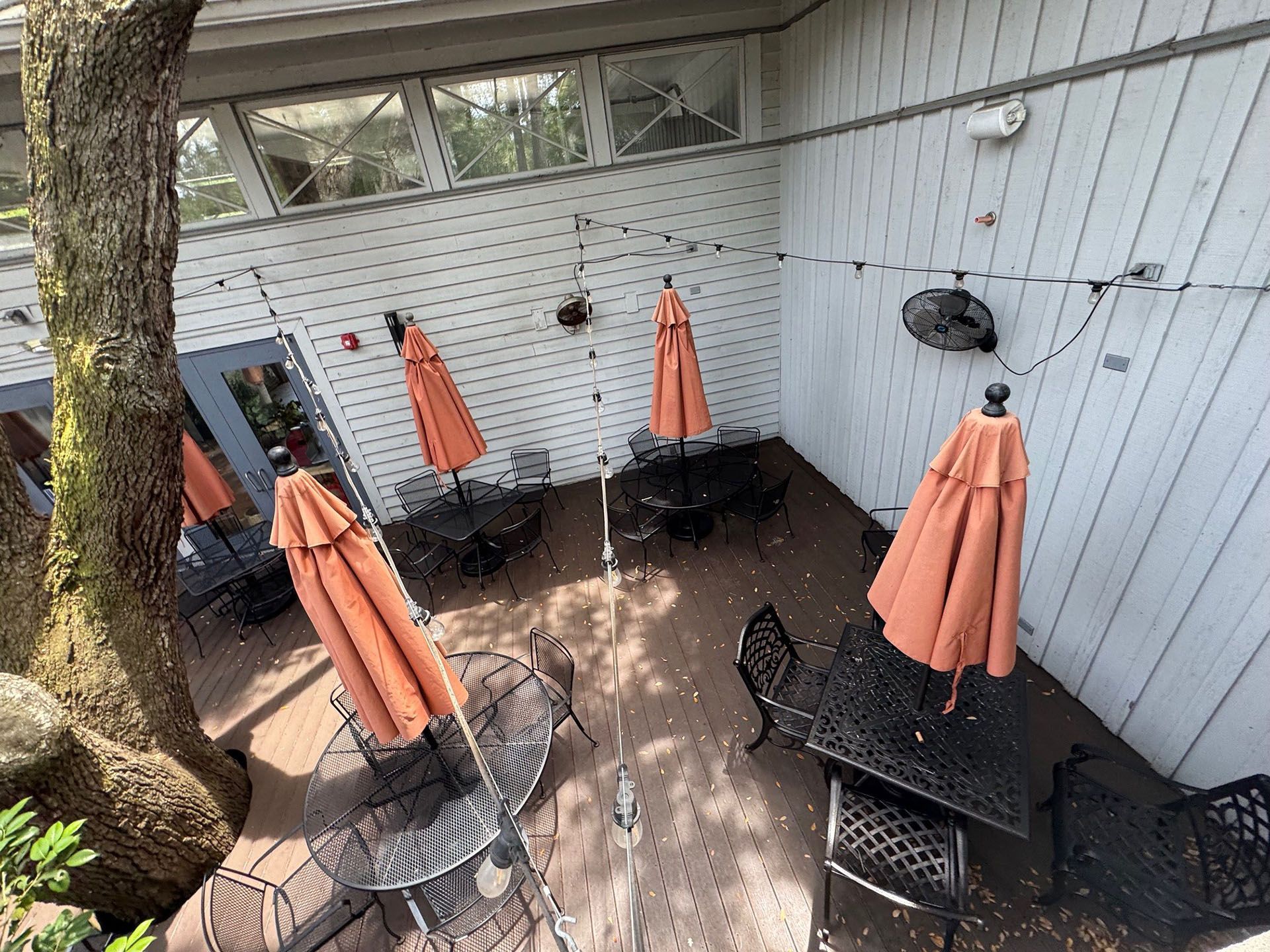 Commercial restaurant remodel and expansion  - Nunzios/Before: Outdoor dining area with tables, umbrellas, and a tree. Orange umbrellas, black tables, and a white building.