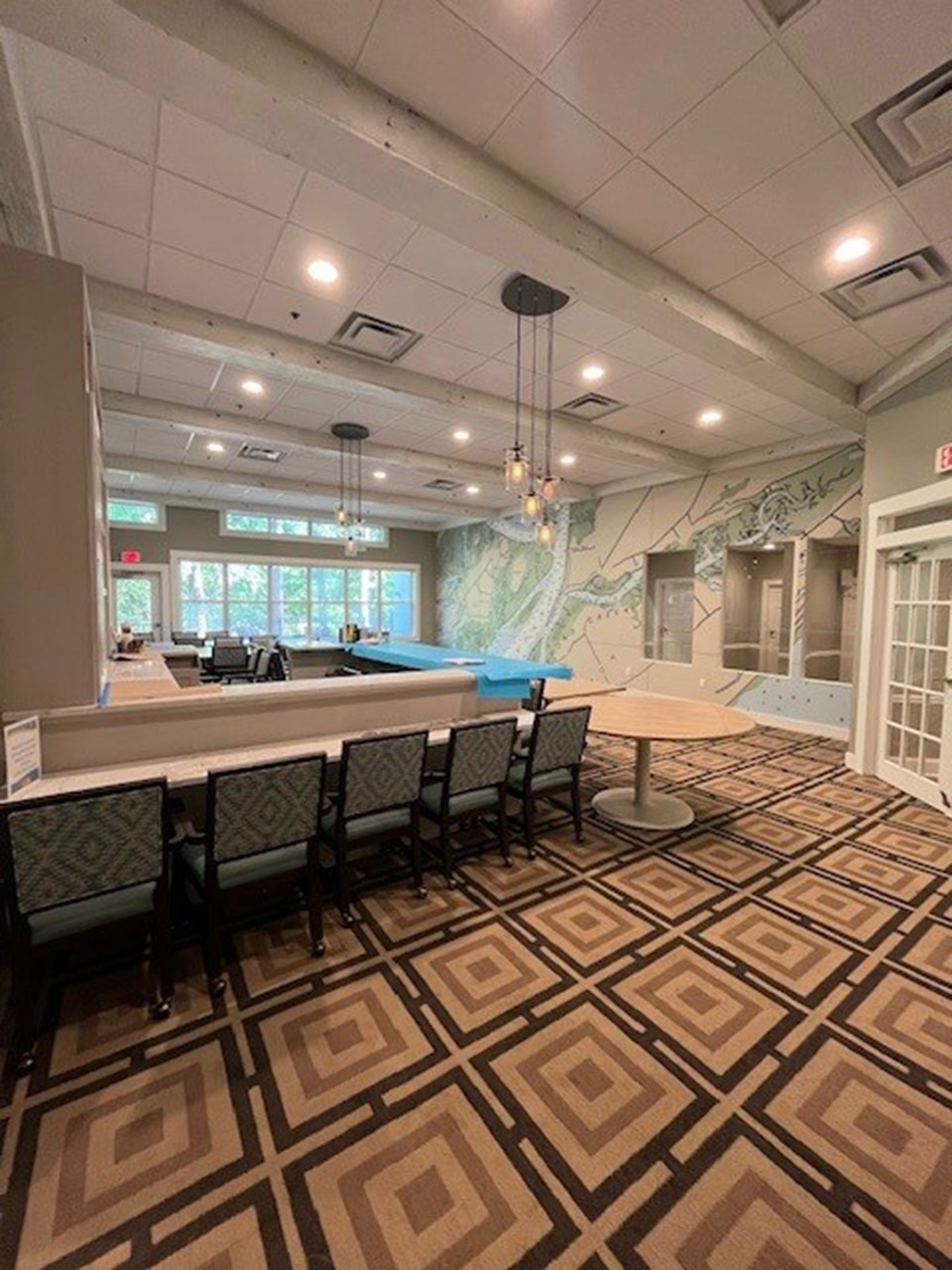 Commercial restaurant remodel and expansion - Tidepoint/After: Spacious room with a bar, chairs, and patterned carpet. Features include a mural and round table.