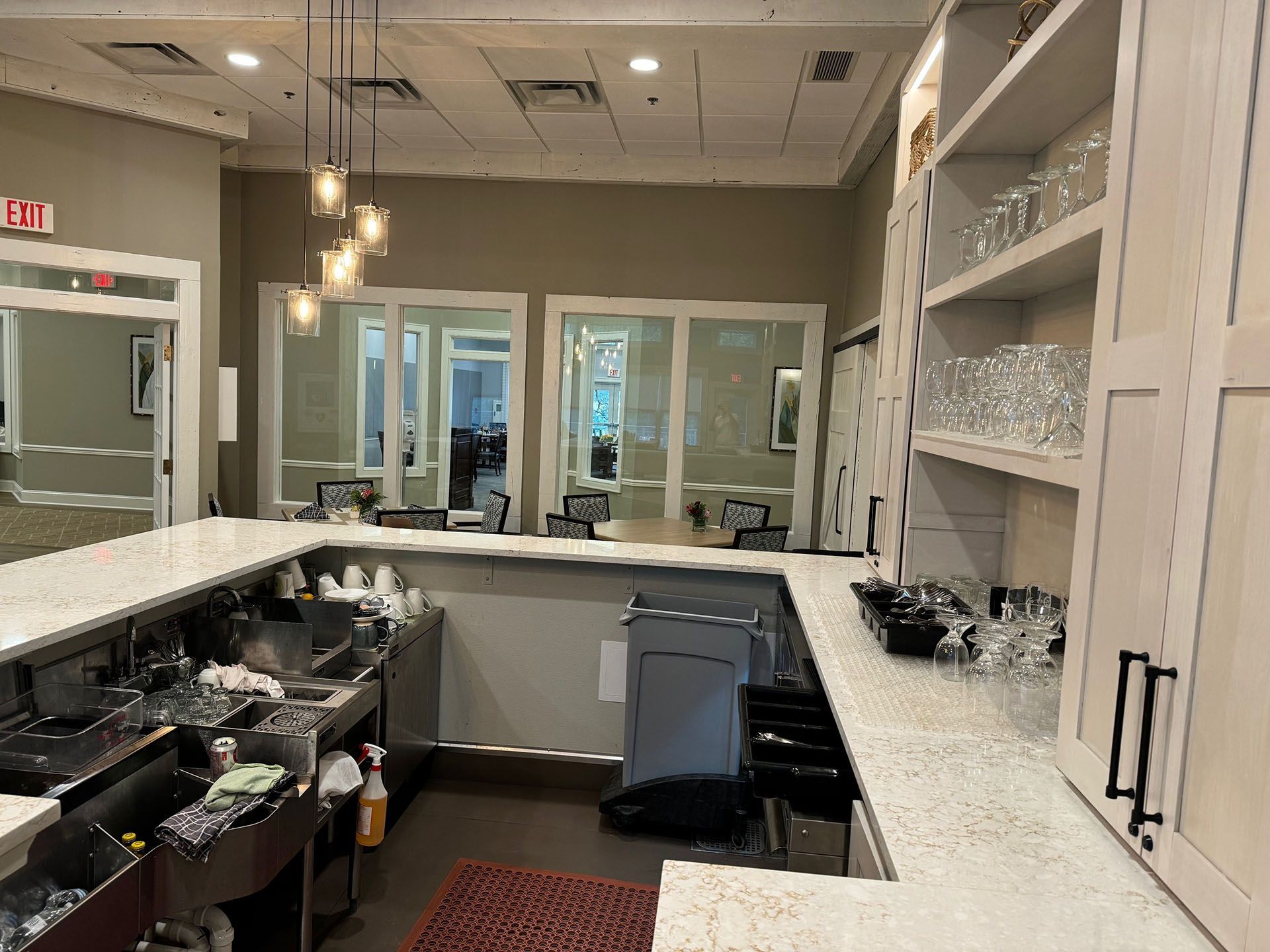 Commercial restaurant remodel and expansion - Tidepoint/After: Interior view of a bar with a white countertop and shelving, glasses, and a doorway with a red 