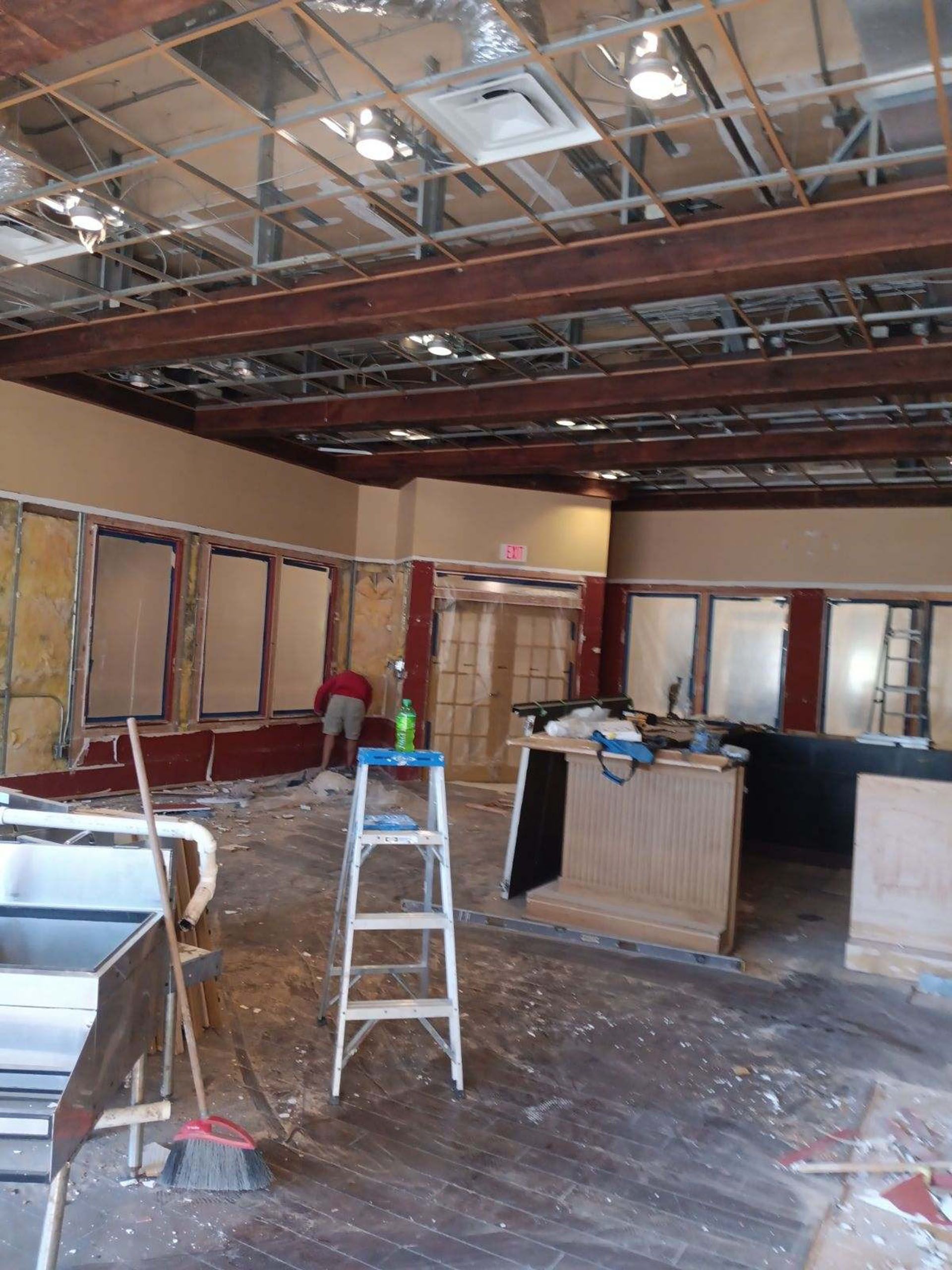 Commercial restaurant remodel and expansion - Tidepoint/During: Interior of a building under construction. A person works on the exposed walls, debris on the floor, and a ladder is in the center.