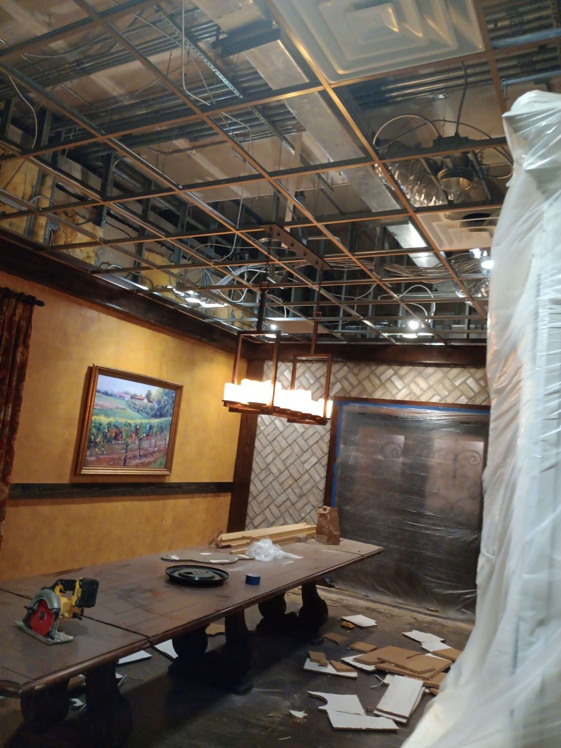Commercial restaurant remodel and expansion - Tidepoint/During: Interior room under construction with exposed ceiling supports, a long table, and a partially covered wall.