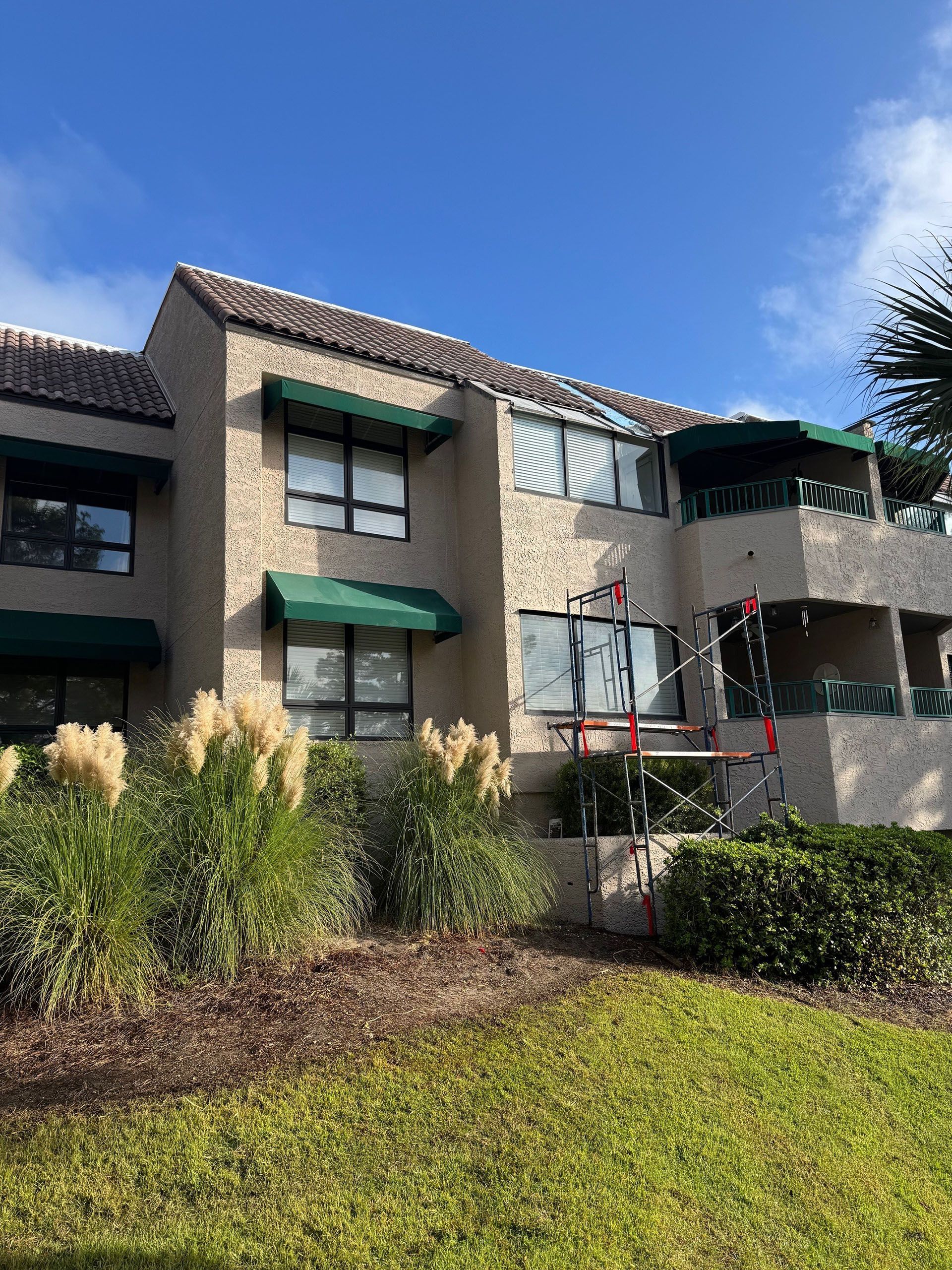 Commercial water damage - After: Beige stucco building with green awnings and a tiled roof, under a blue sky.