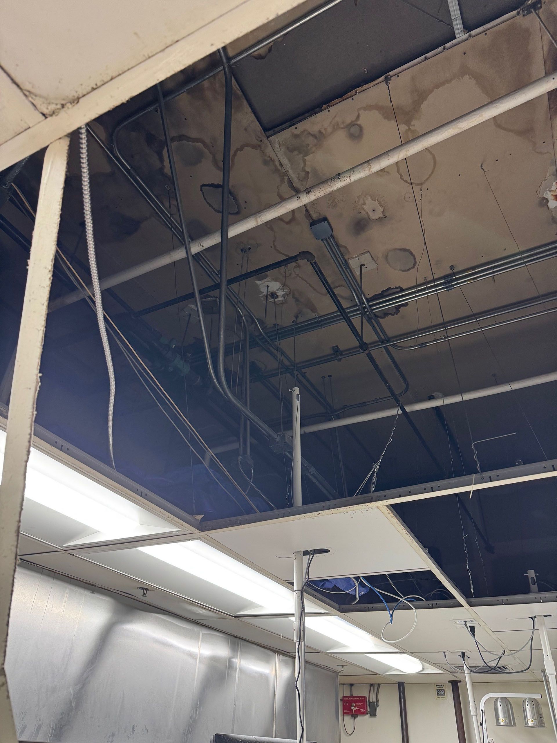 Commercial water damage - Before: Interior ceiling with exposed wires and panels in a commercial or industrial space.