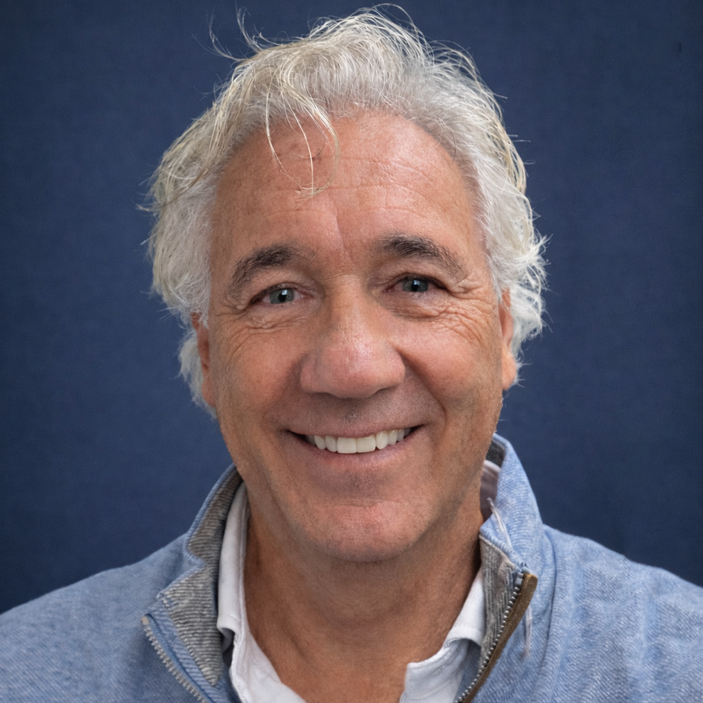Smiling man with gray hair, wearing a light blue zip-up sweater against a blue background.