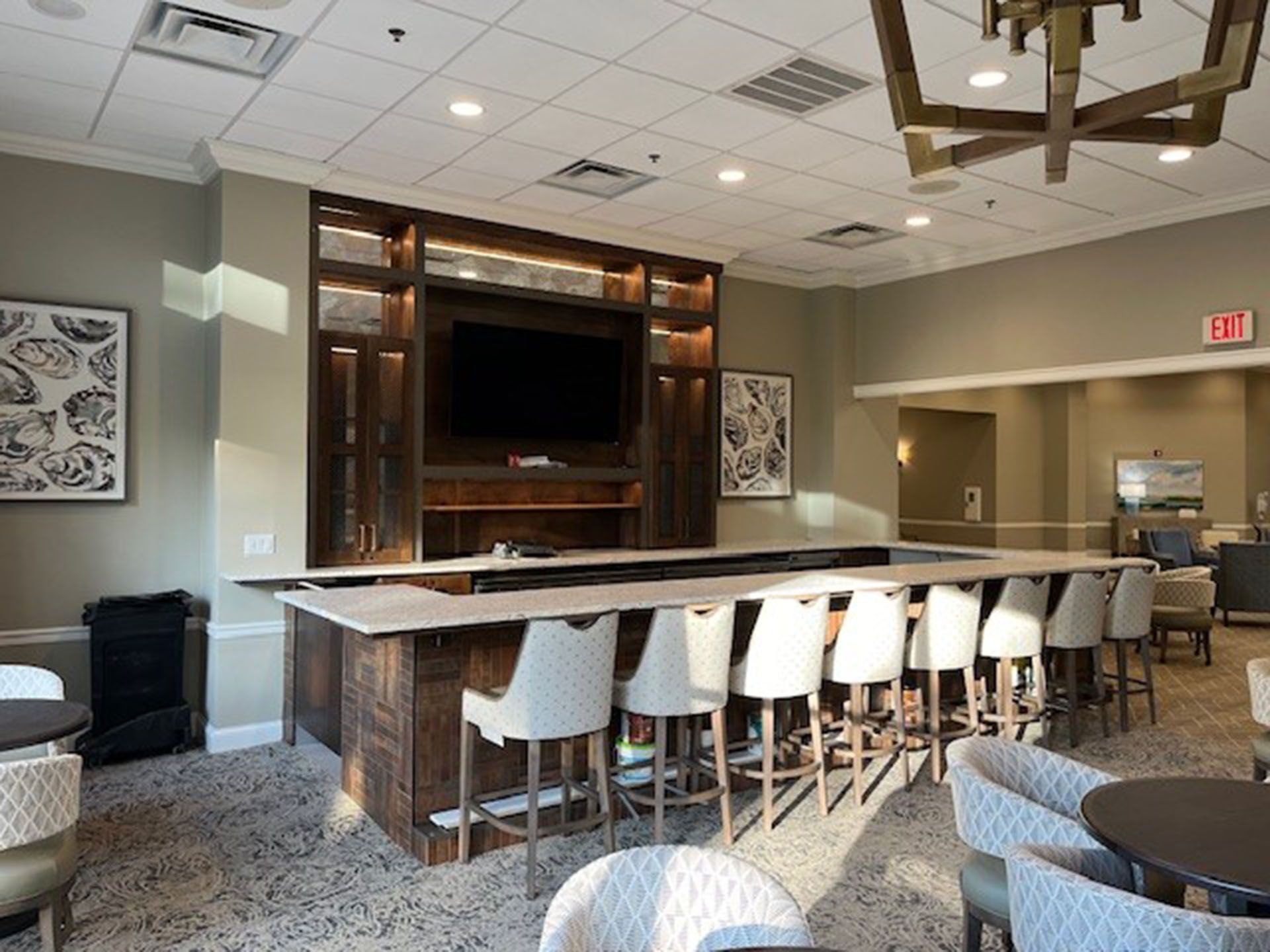 Commercial bar remodel - Bar area with TV, seating at the counter and tables. Brown wood, white seating, neutral walls, and patterned flooring.