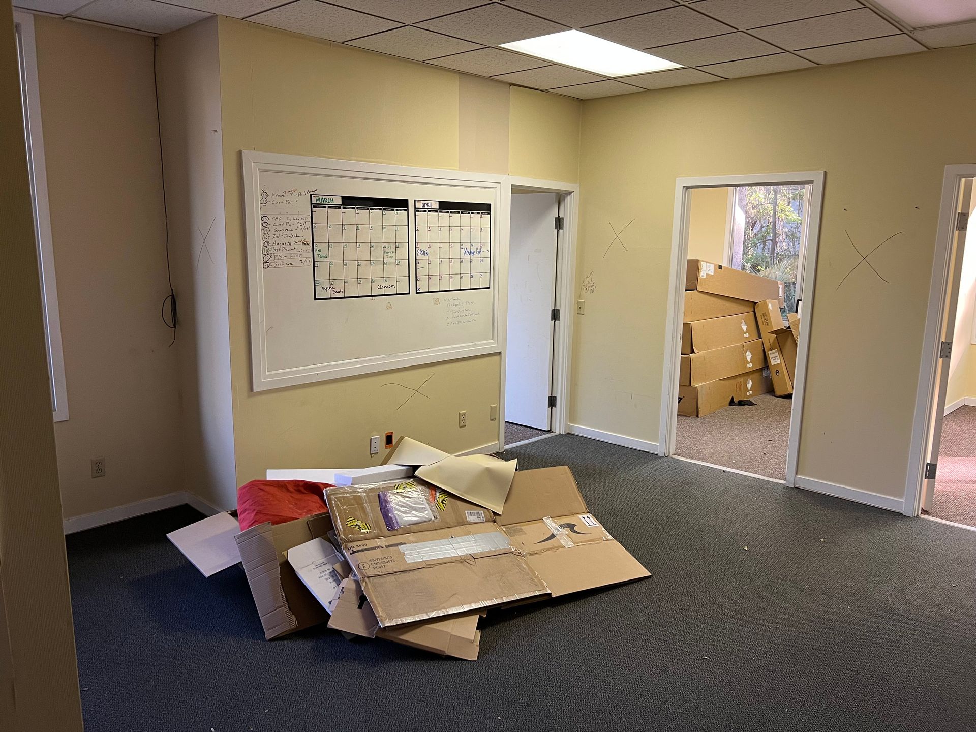 Empty office space with scattered cardboard boxes, a whiteboard, and three open doorways.