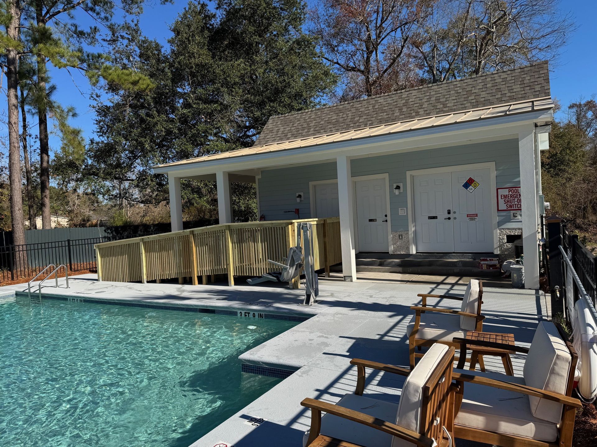 Poolside building with two changing rooms and seating area. Pool in foreground with a ramp leading up.