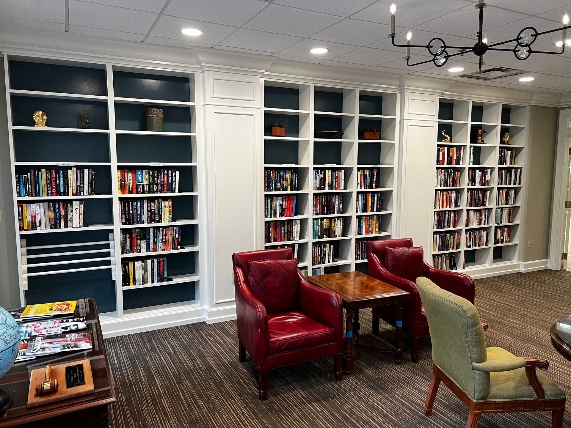 Library seating area with built-in bookshelves, red armchairs, and a small table.