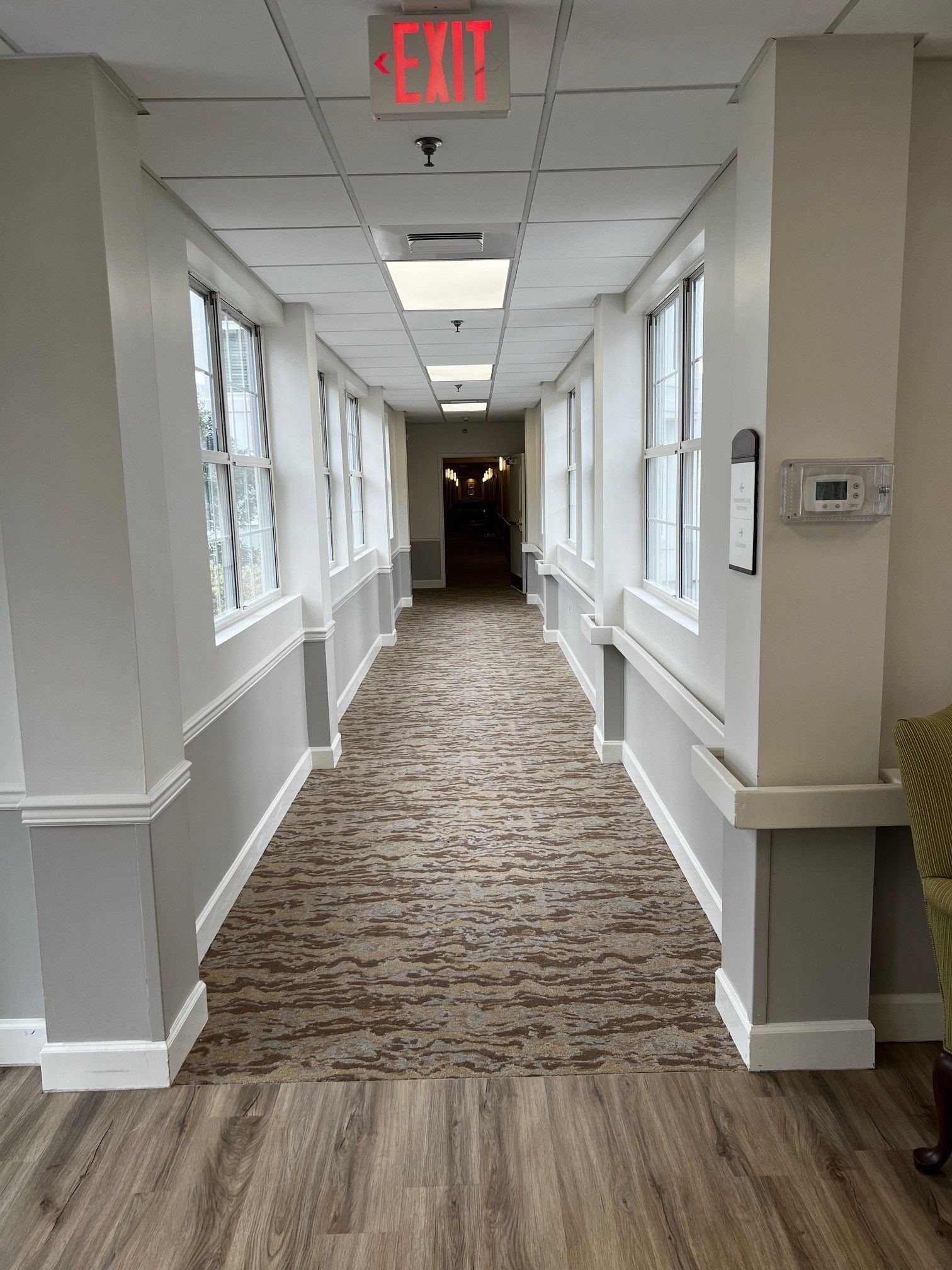 Hallway with windows, an exit sign, and a textured carpet.