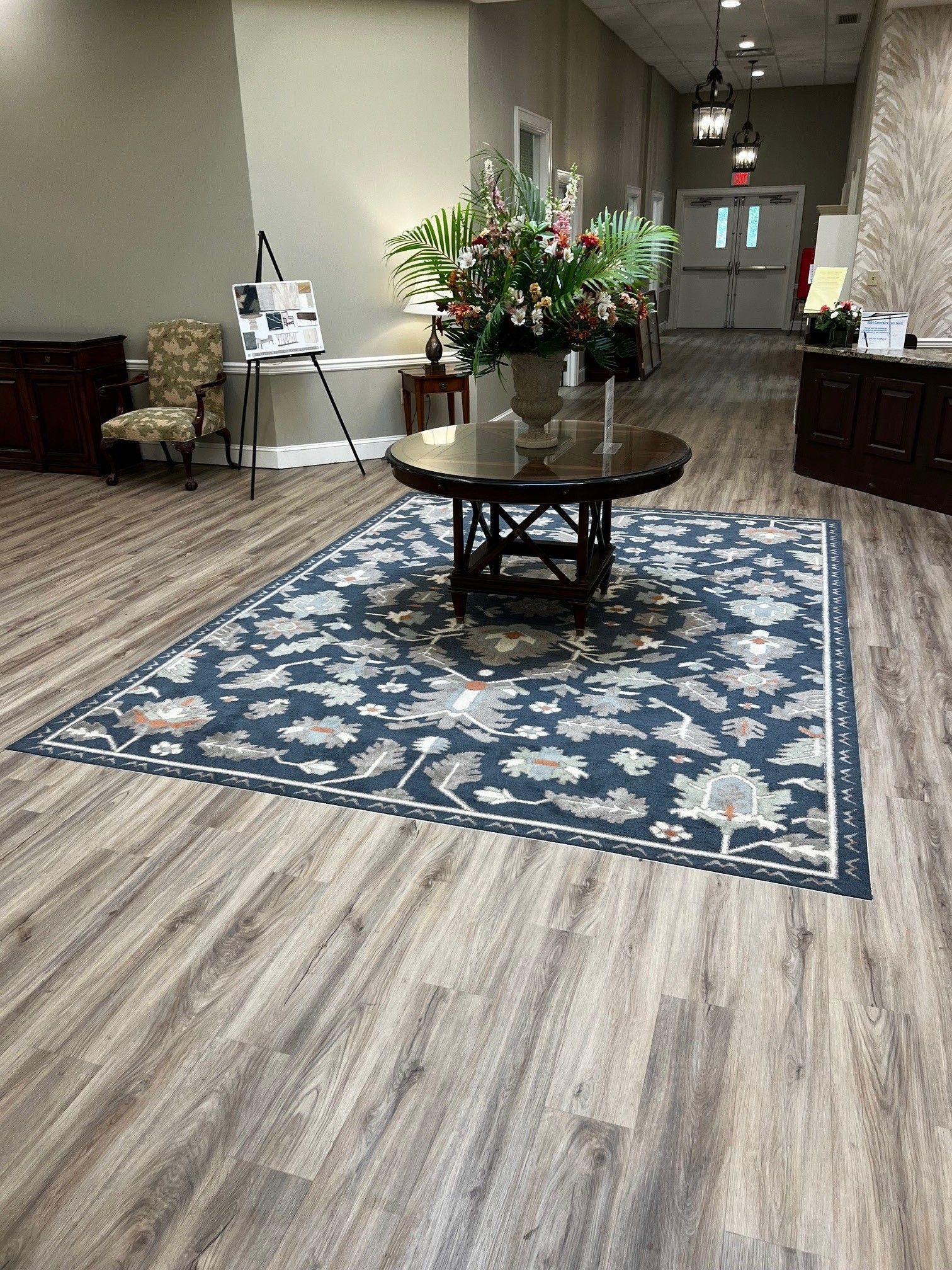 Lobby with patterned rug, round table holding a floral arrangement, light wood flooring, and various furnishings.