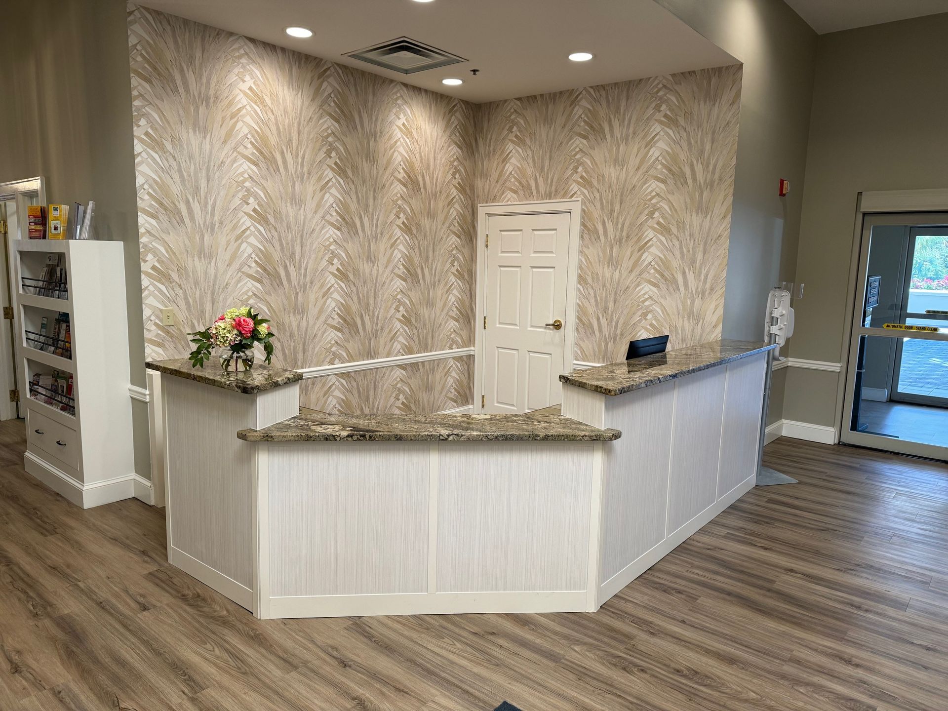 Reception desk with beige granite countertop, white paneling, and tan patterned wallpaper.