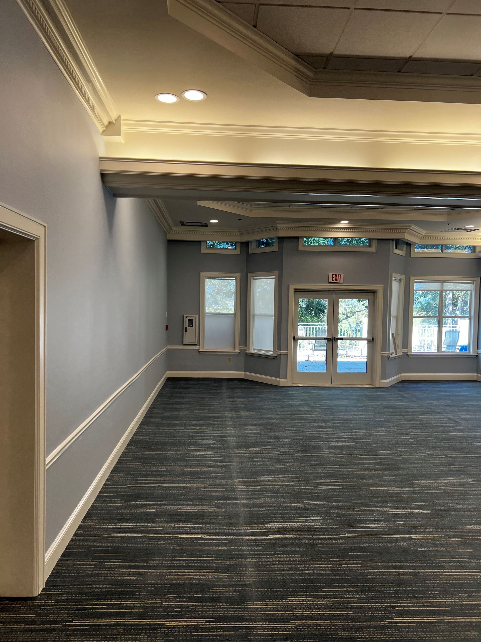 Empty room with blue walls, carpet, and decorative ceiling, leading to exterior doors and windows.