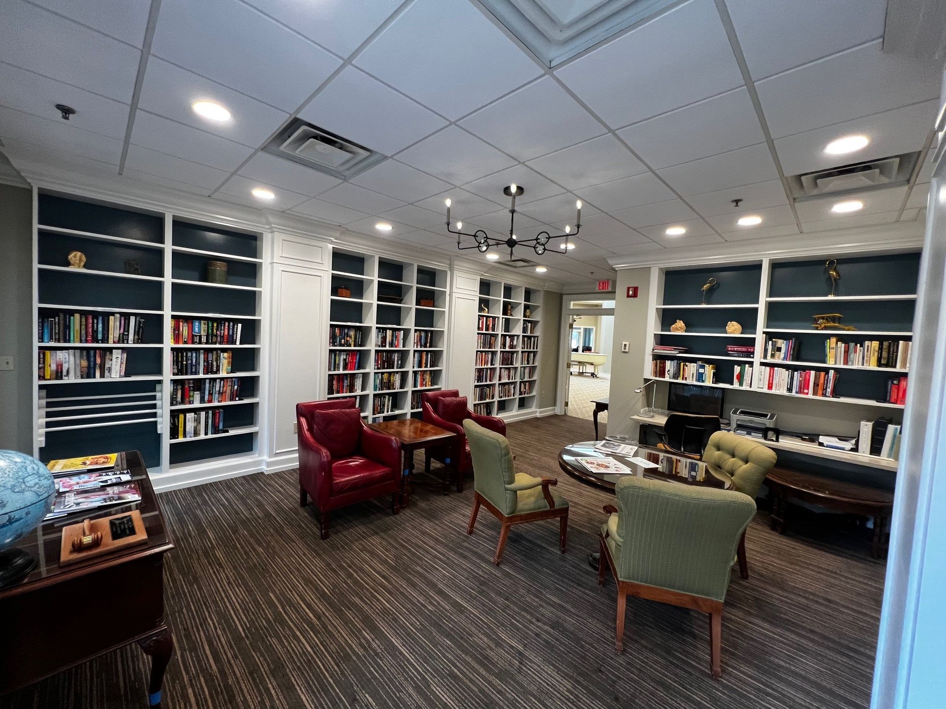 Cozy library with bookshelves filled with books, seating areas with chairs, and a small table.