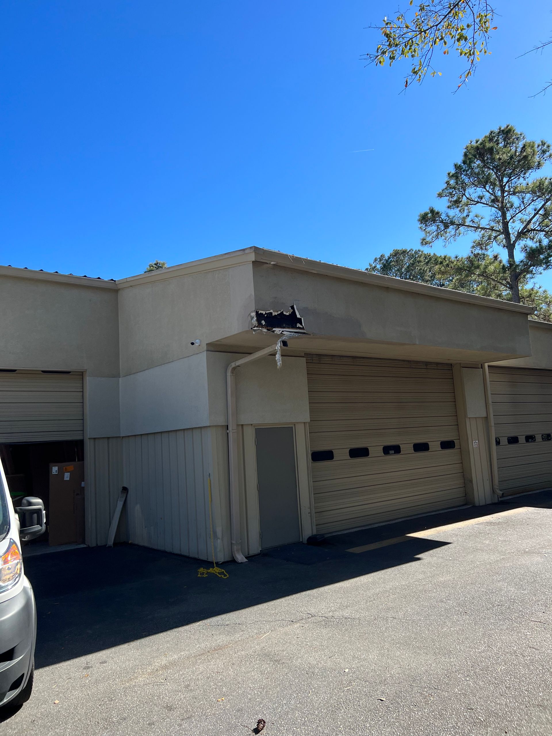 A building with garage doors, a clear blue sky, and a tree. A security camera is mounted above a door.
