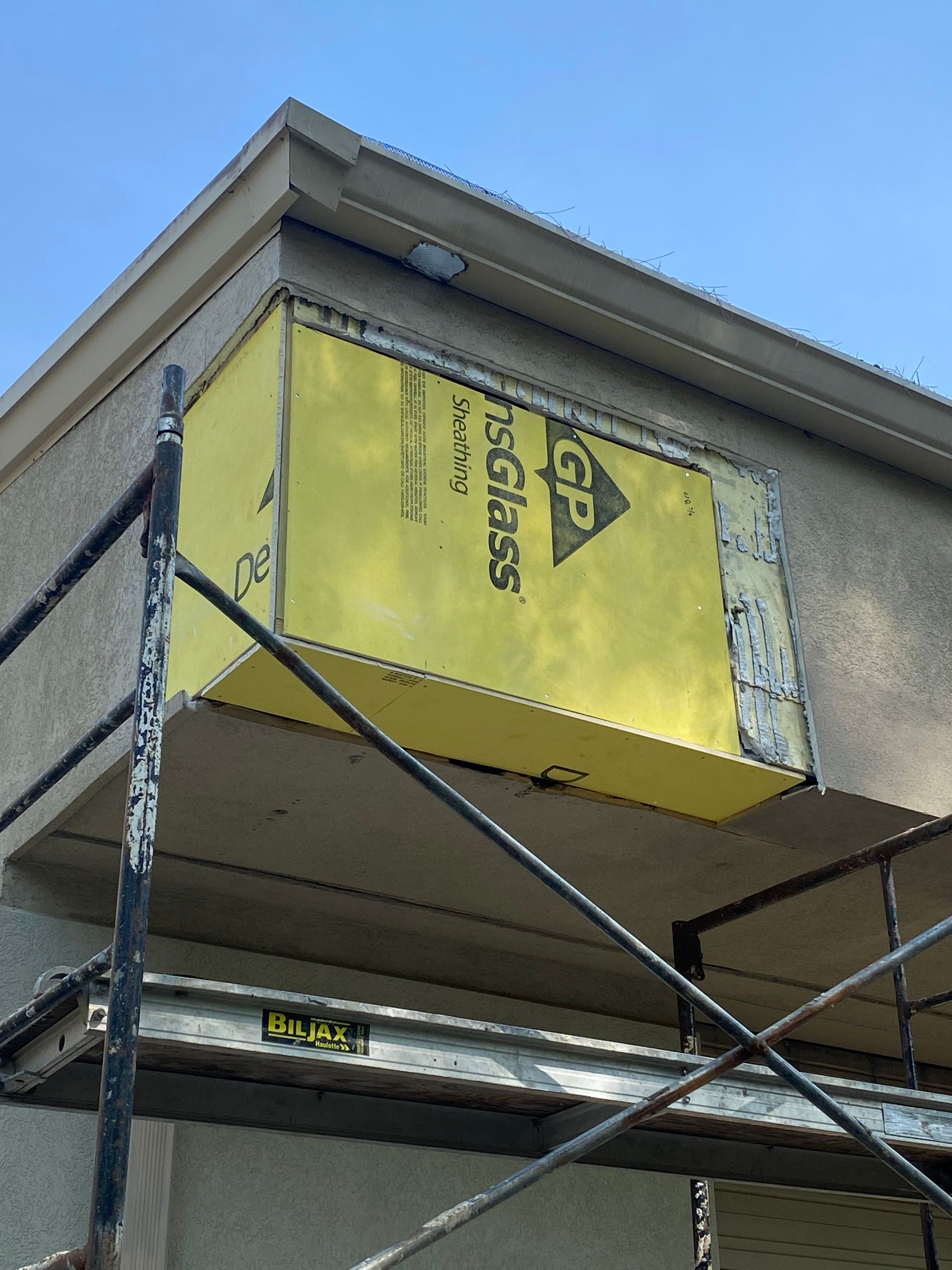 Yellow sheathing on a building exterior, above scaffolding; sky in background.