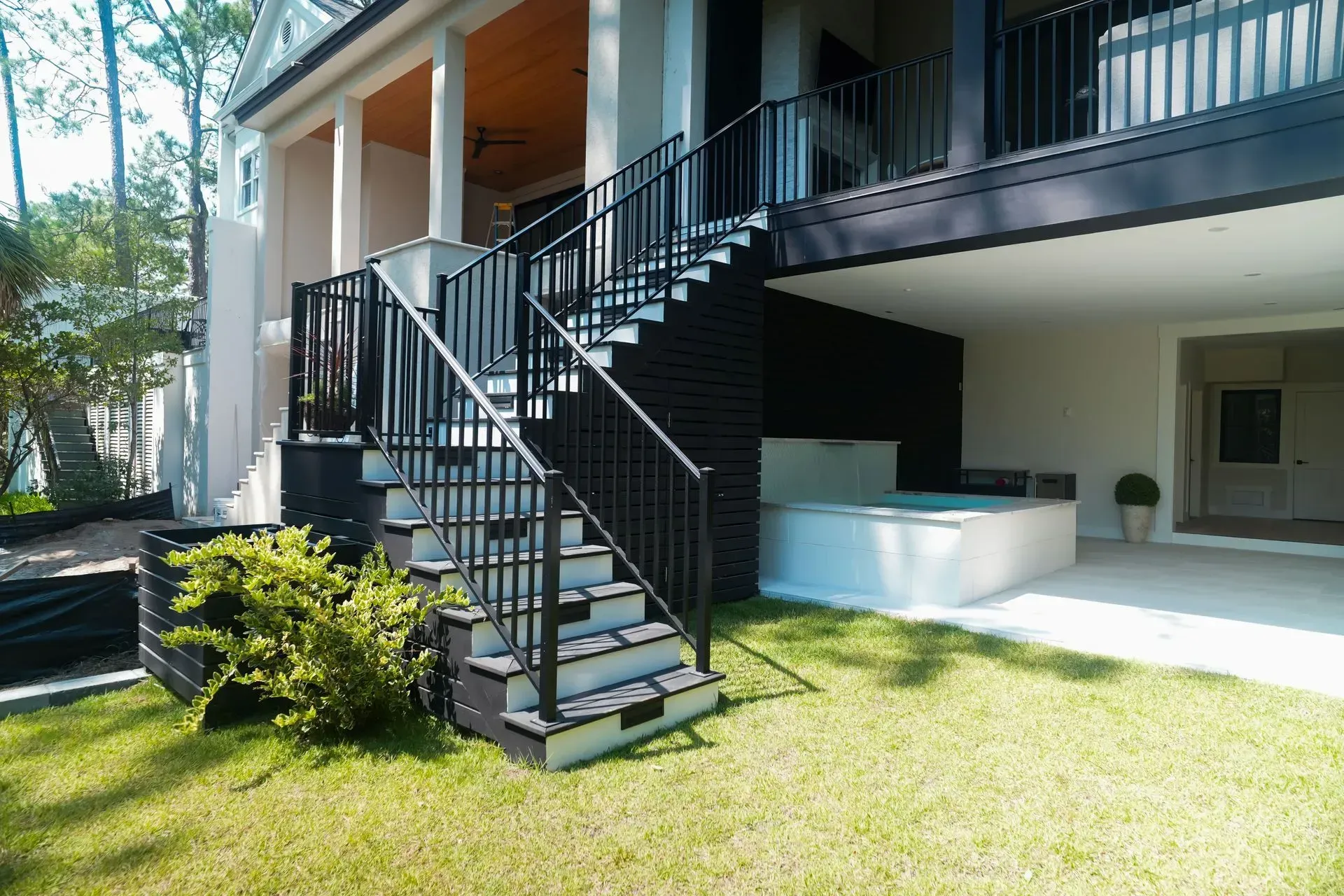 Exterior stairs with black railing leading up to a porch. Below, a small jacuzzi and seating area.