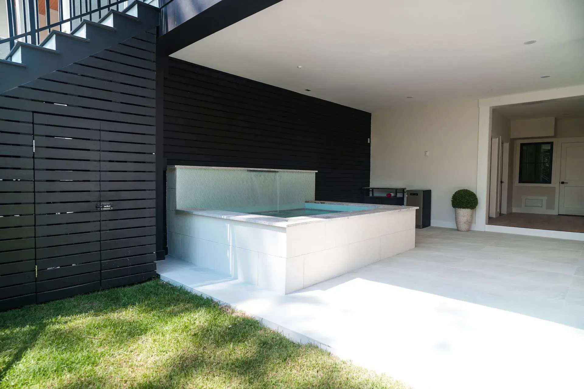 A modern outdoor space with a hot tub, grass, and a black wall.