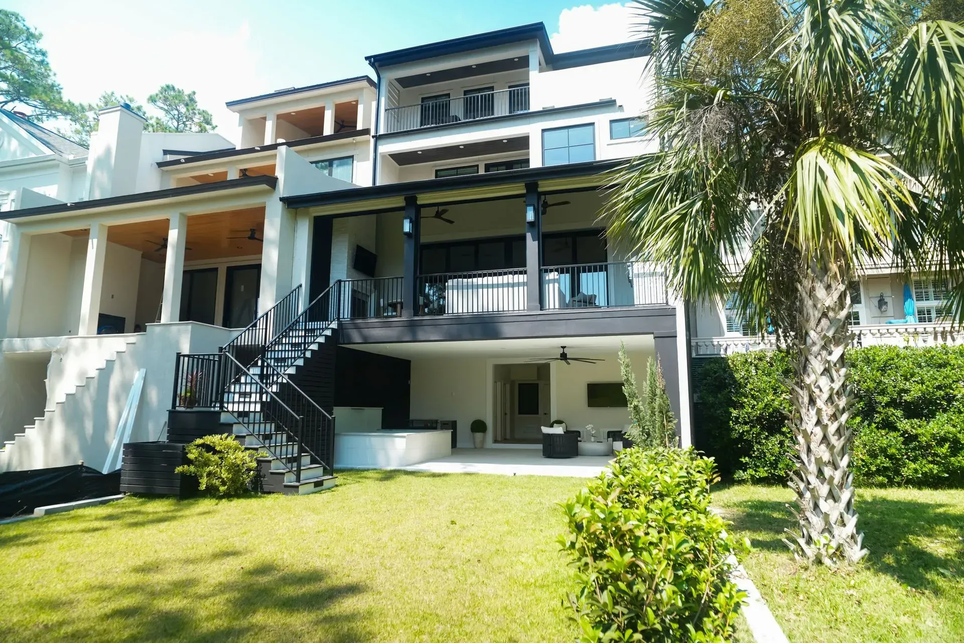 Multi-story modern home with balconies, black railings, and palm tree.