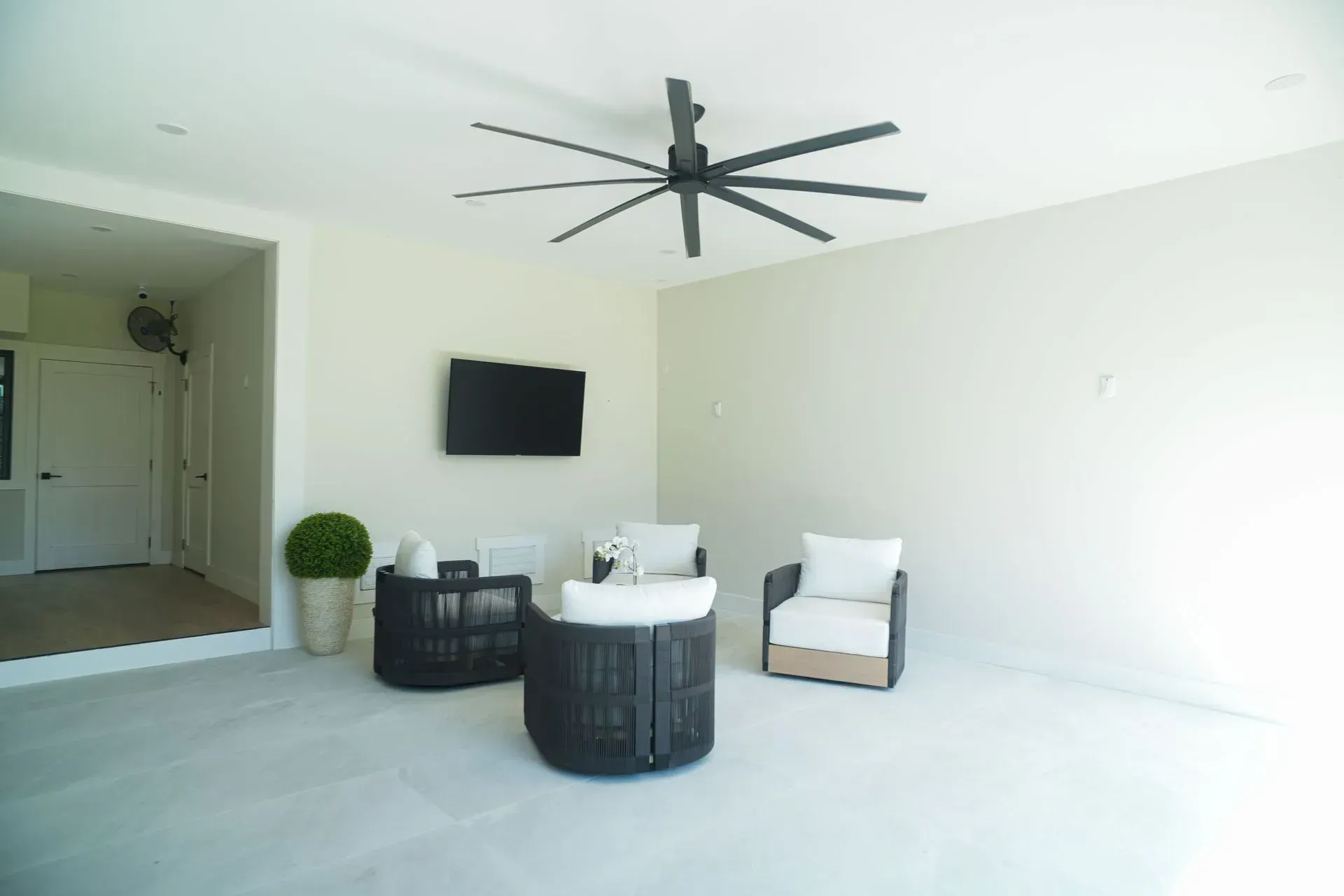 Patio seating area with a ceiling fan, TV, and cream-colored walls and flooring.