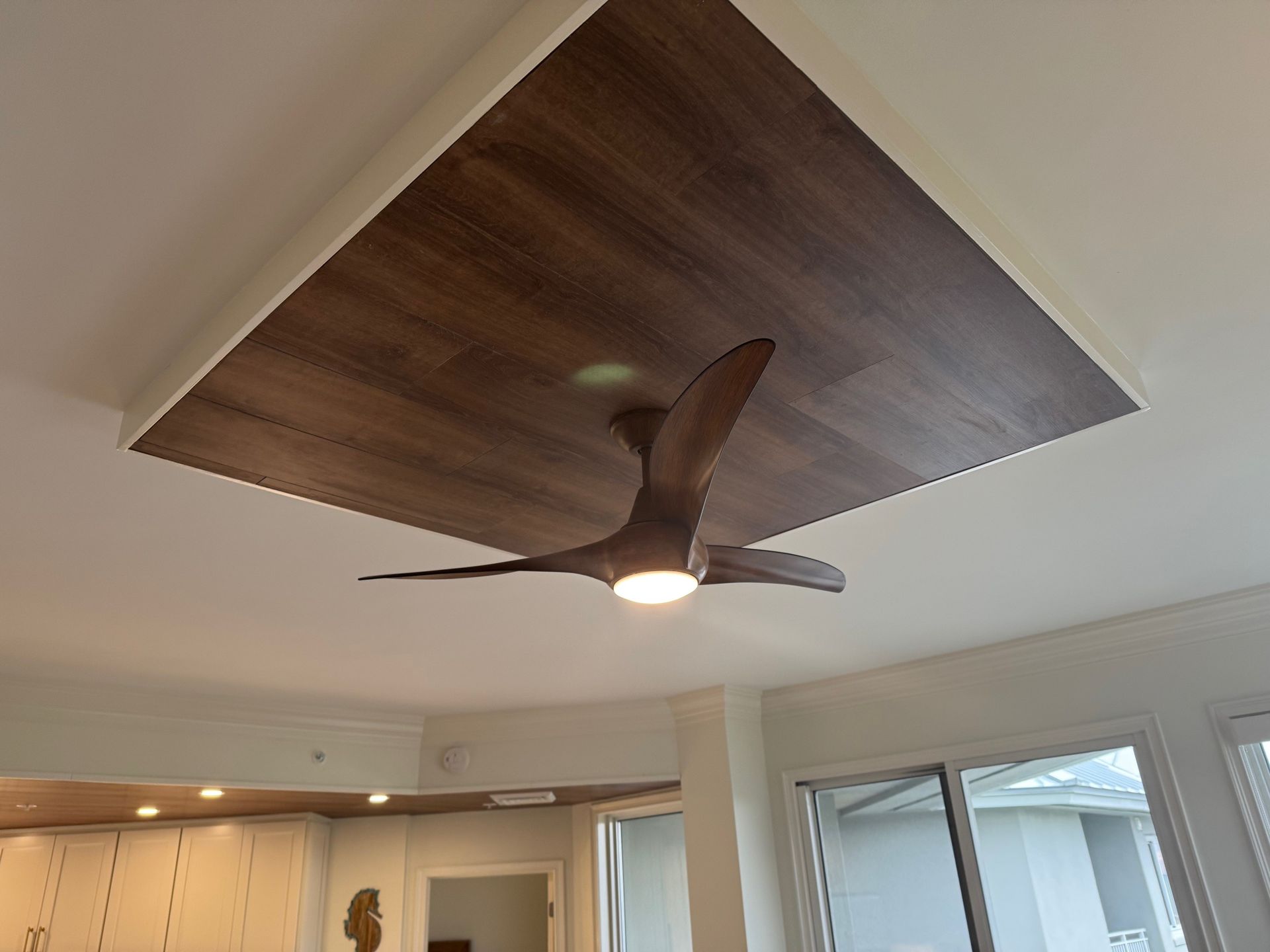 Ceiling with dark wood paneling, a ceiling fan, and recessed lighting. White trim frames the panel.