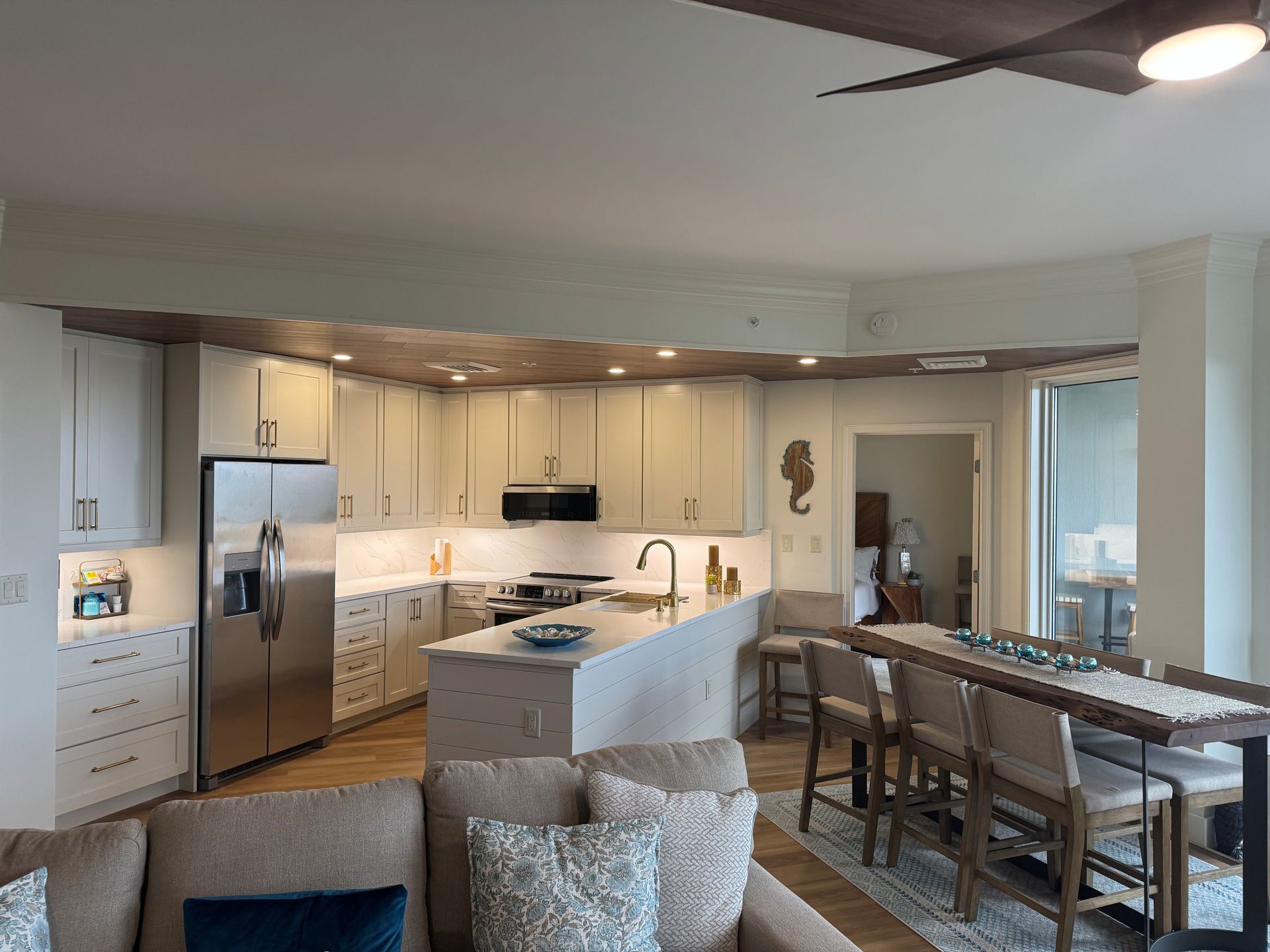 Open-concept kitchen with white cabinets, stainless steel fridge, island, dining table, and living room seating.