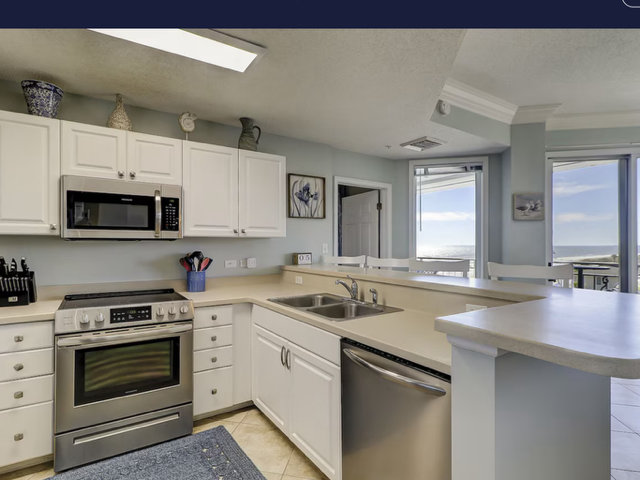White kitchen with stainless steel appliances, light countertops, and ocean view.