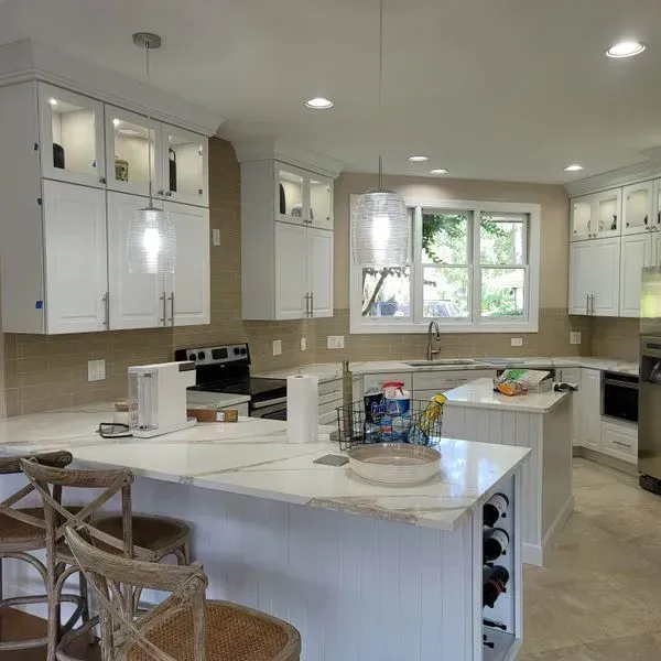 White kitchen with a marble countertop island and cabinetry, light-colored walls, and pendant lights.
