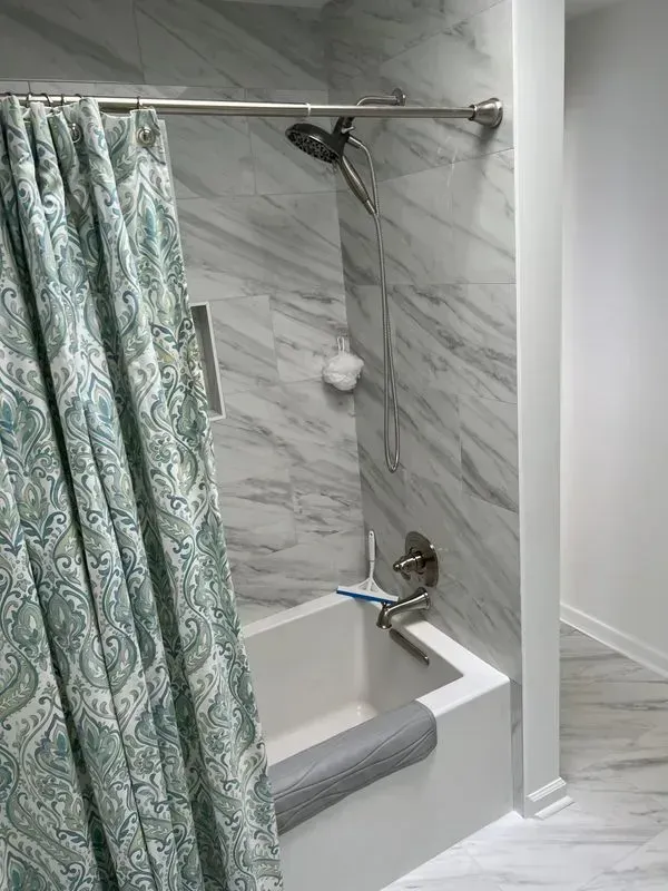 Bathroom with white tub, marble tile, and blue and white paisley shower curtain.