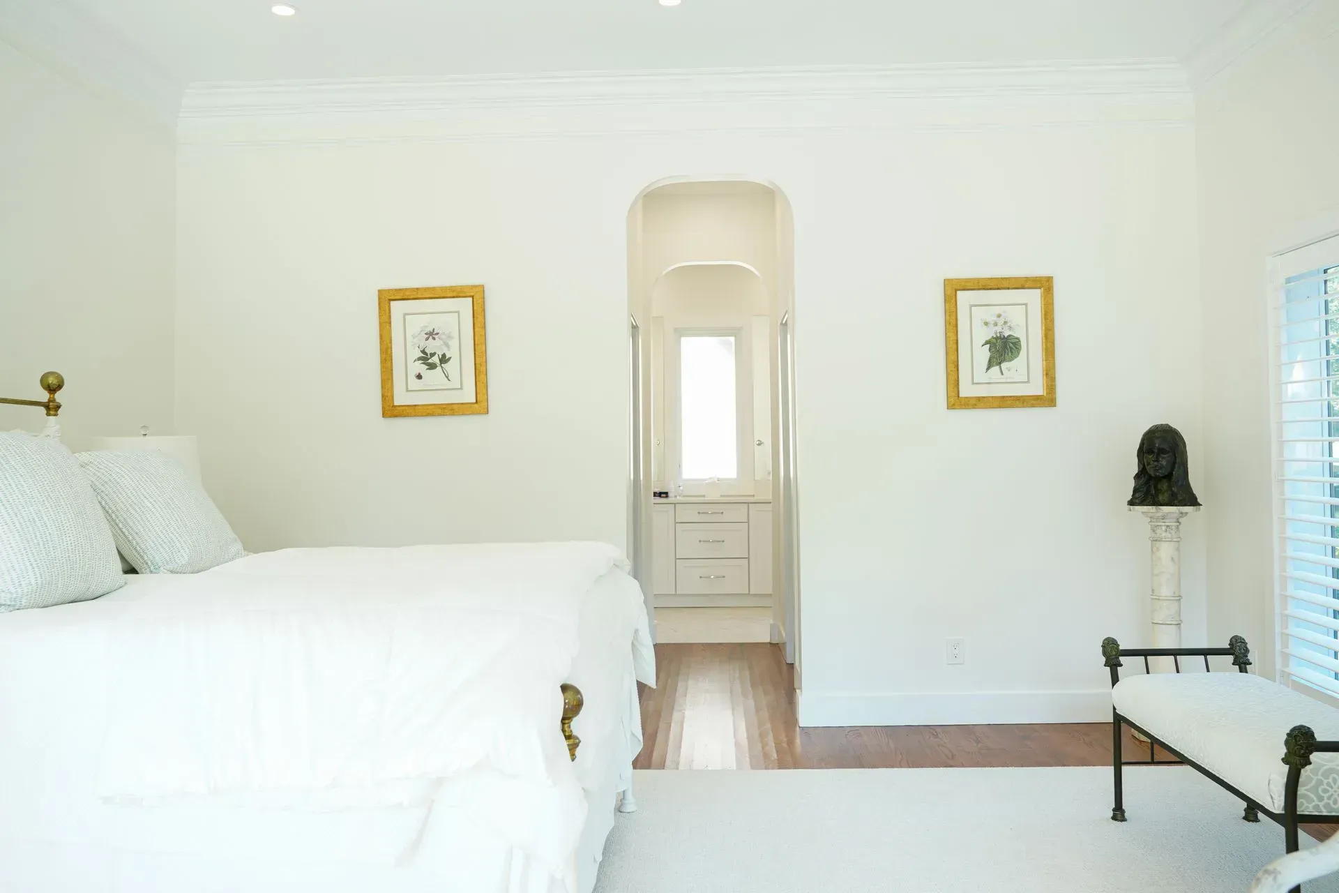White bedroom with bed, artwork, and doorway leading to another room.