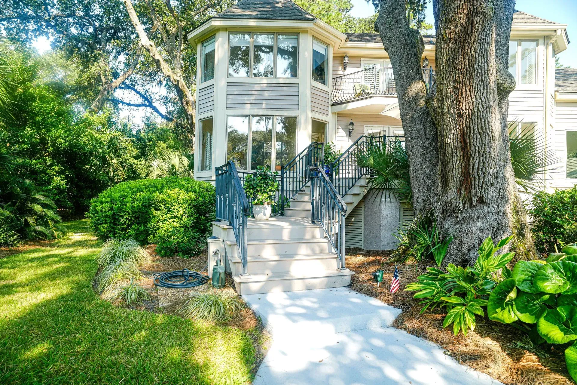 House with multiple stories, light exterior, stairs, and lush greenery in front.