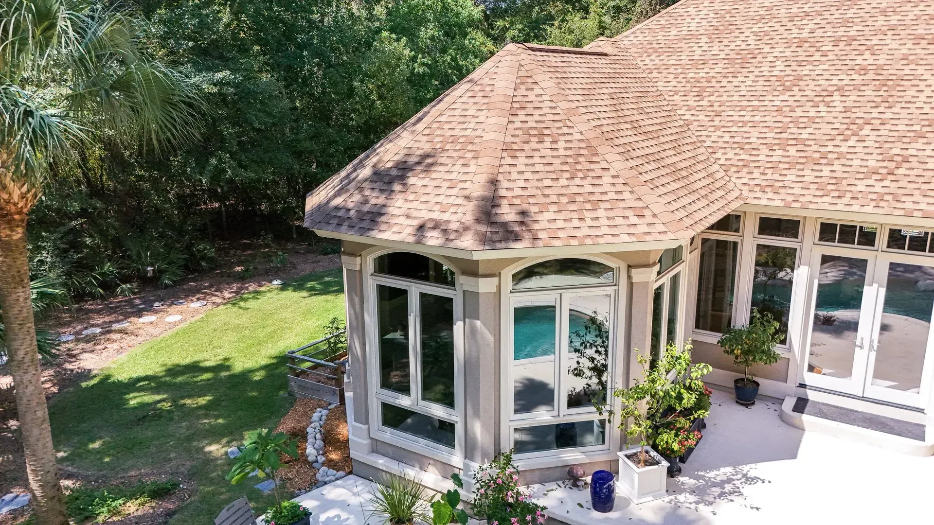 Tan roofed house with many windows surrounded by lush greenery.