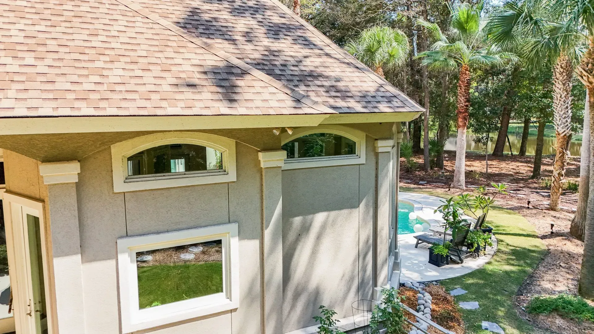 Tan stucco building with arched windows, brown roof, and swimming pool in the background.
