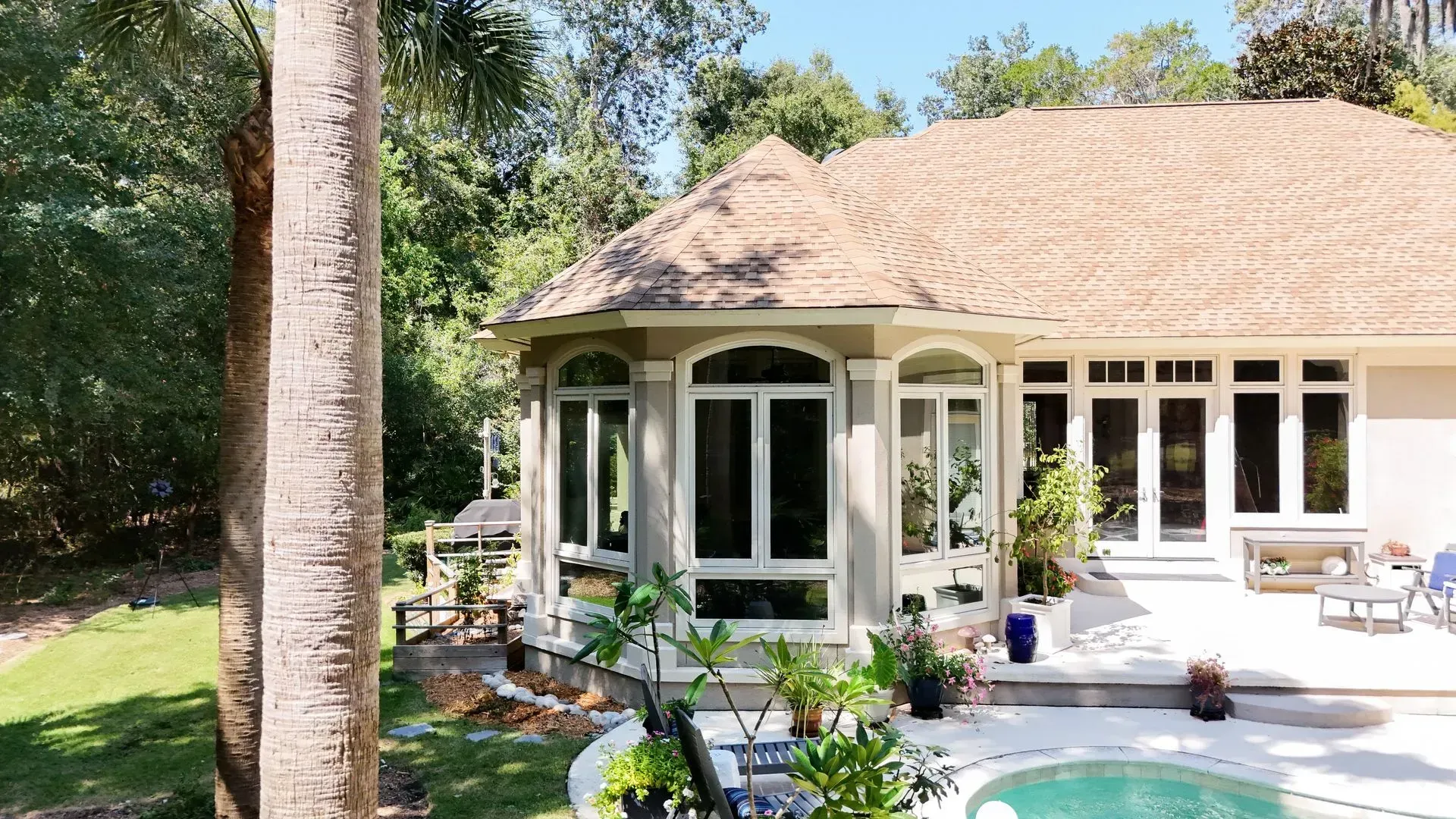 House with large windows and a pool, surrounded by greenery.