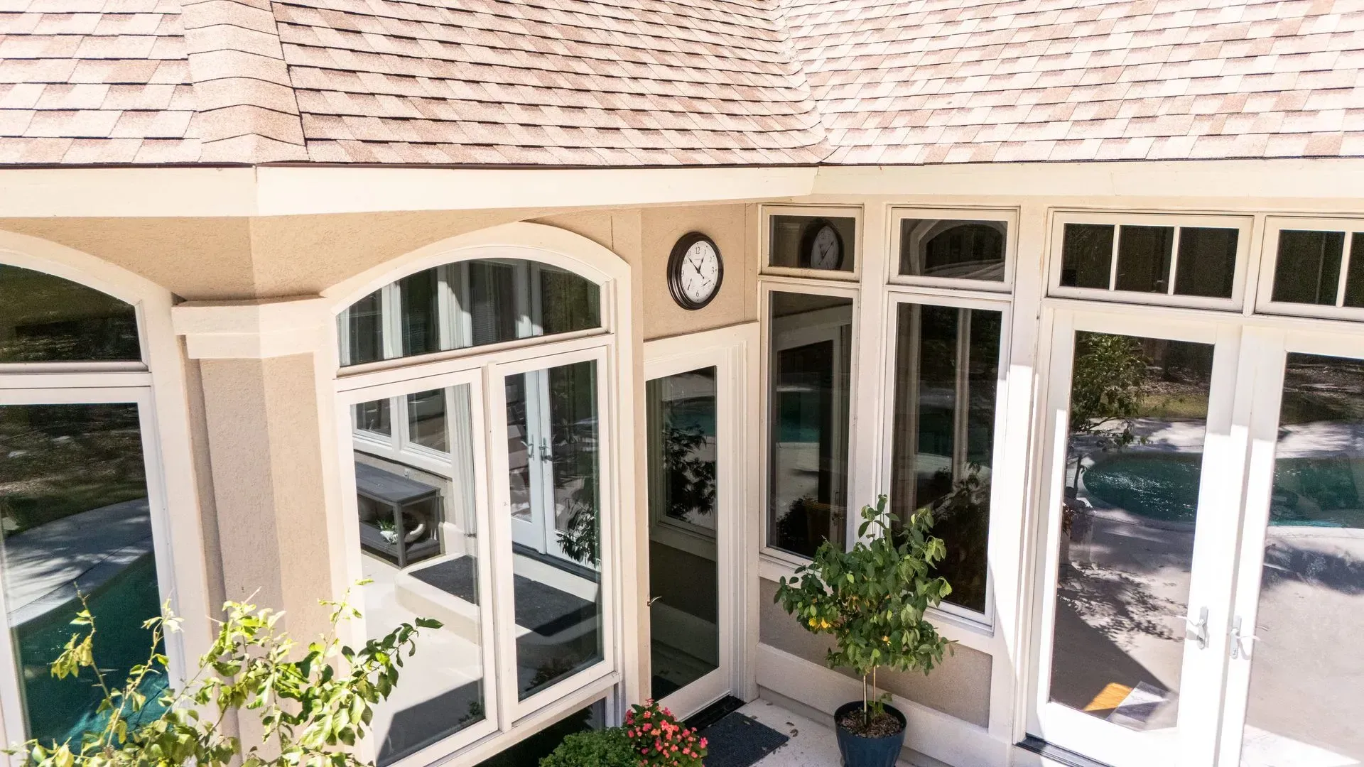 Exterior view of a building with multiple glass doors and windows, beige stucco, a clock, and a tile roof.