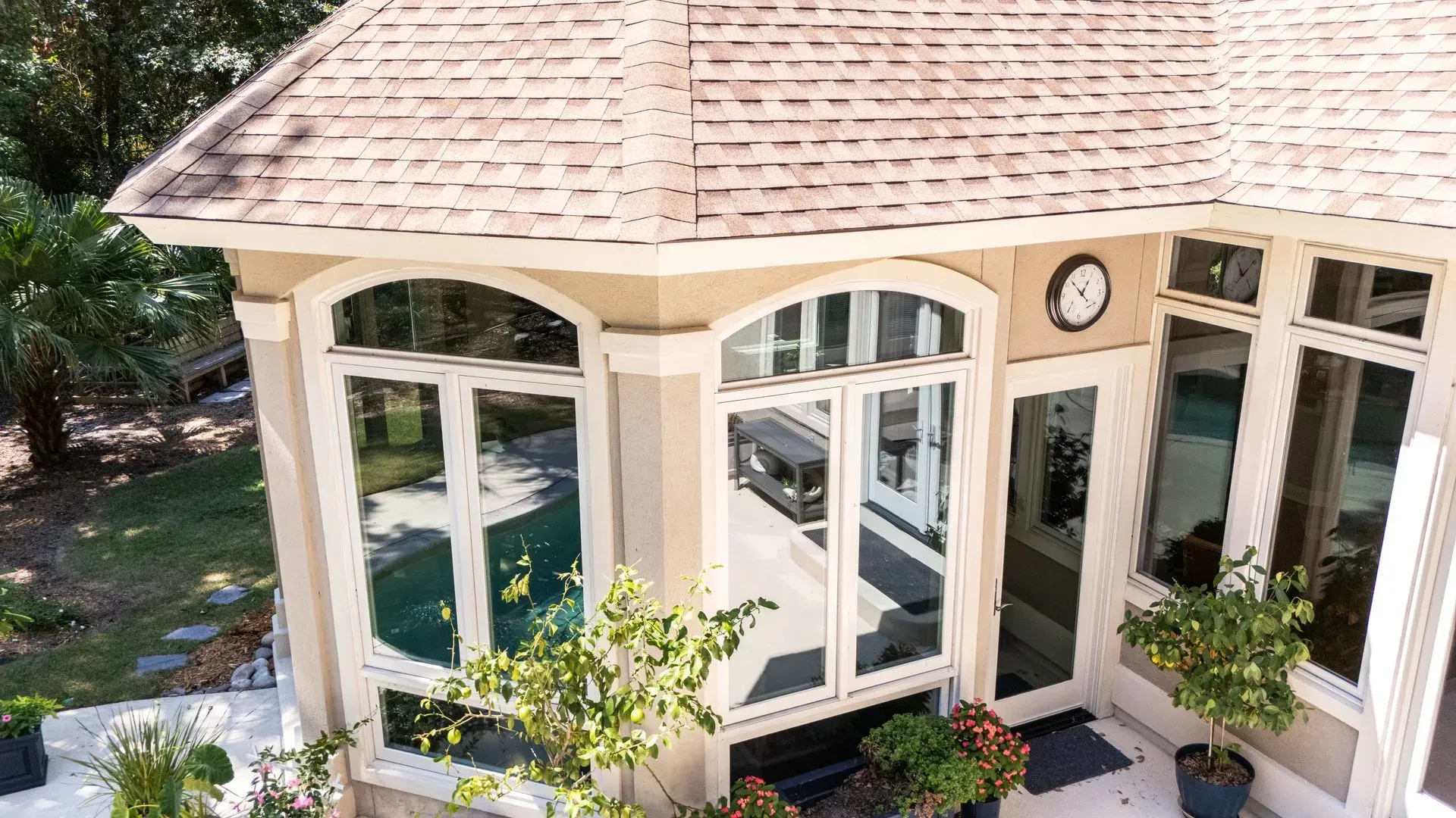 Exterior view of a house with large windows, a light brown roof, and potted plants on the patio.