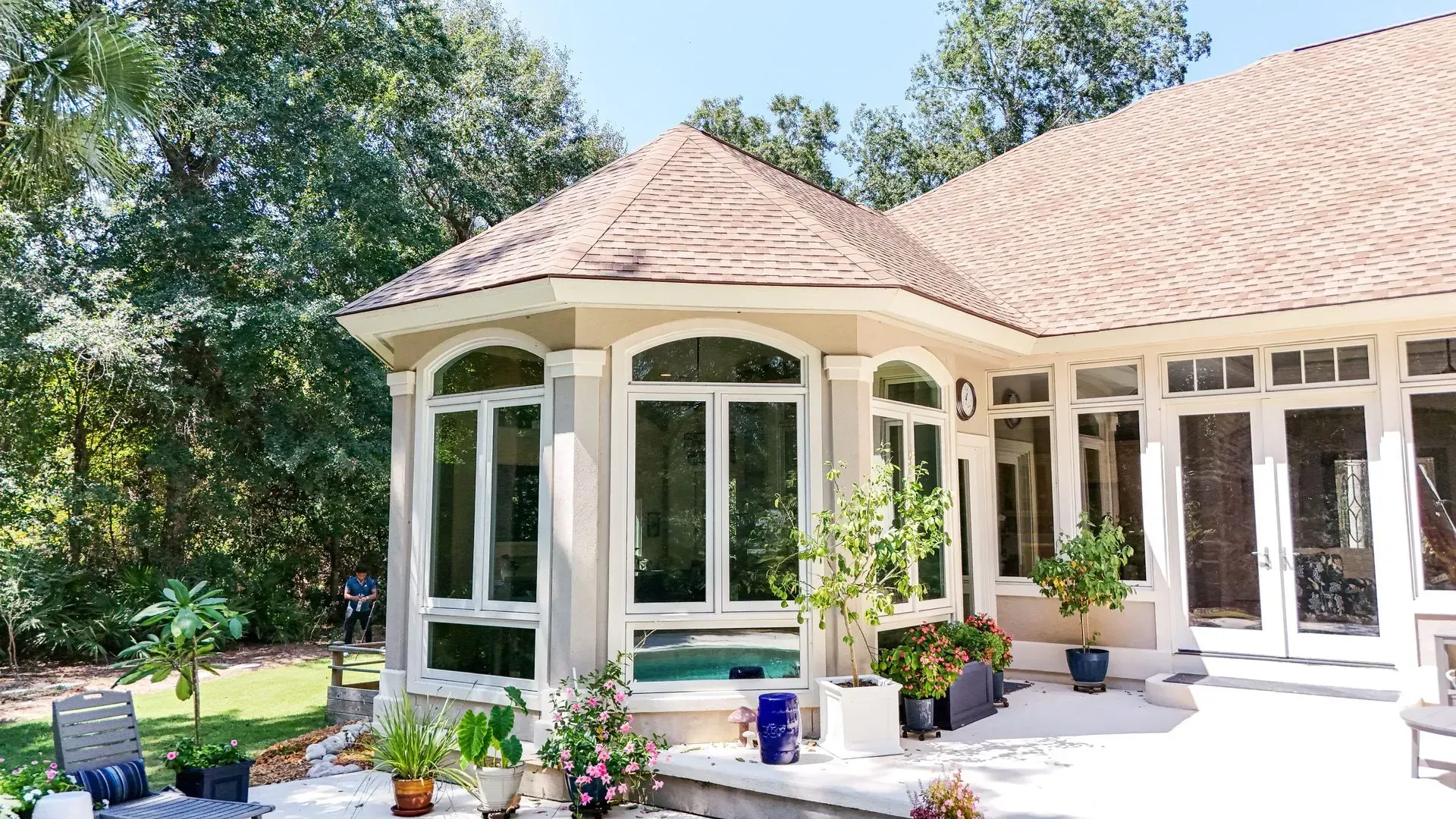 Exterior view of a house with many windows and a patio, surrounded by trees under a blue sky.