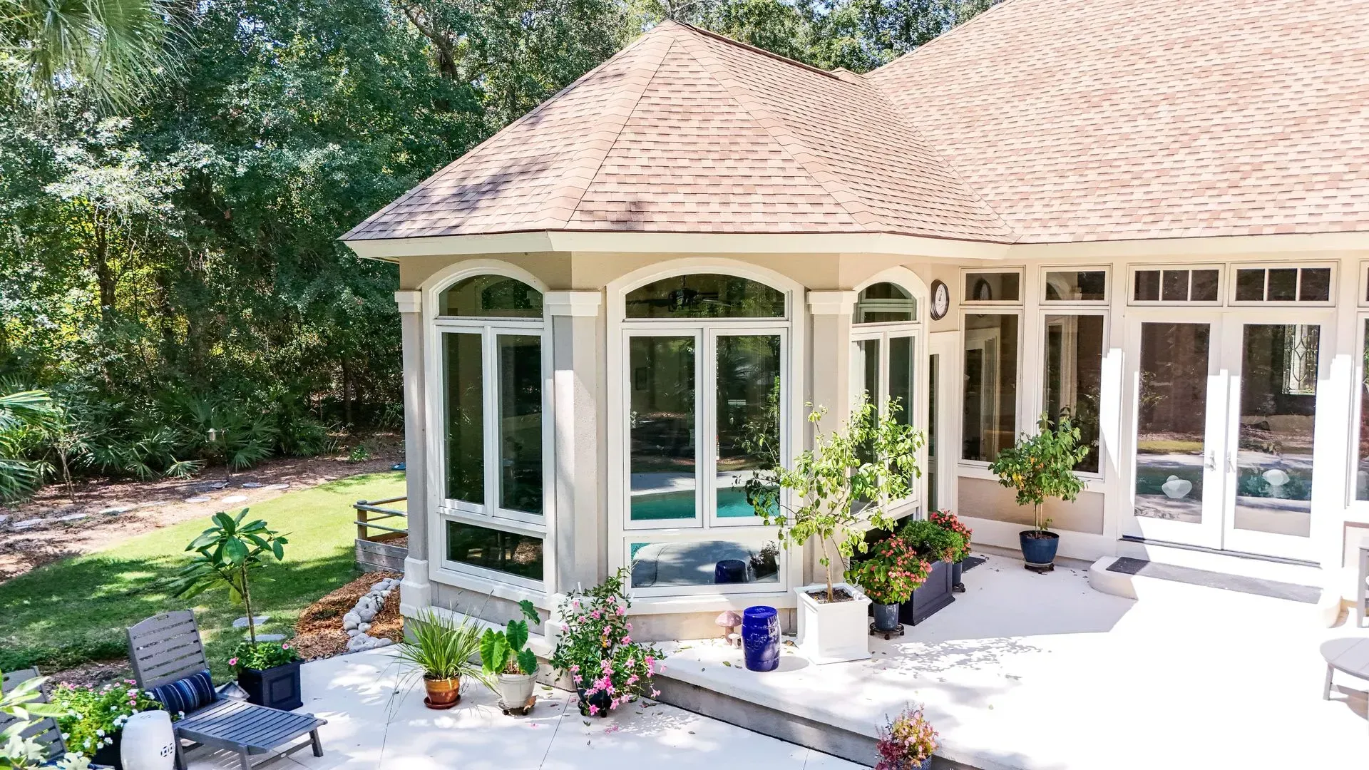 Exterior view of a house with a curved roof, large windows, and a patio with potted plants.