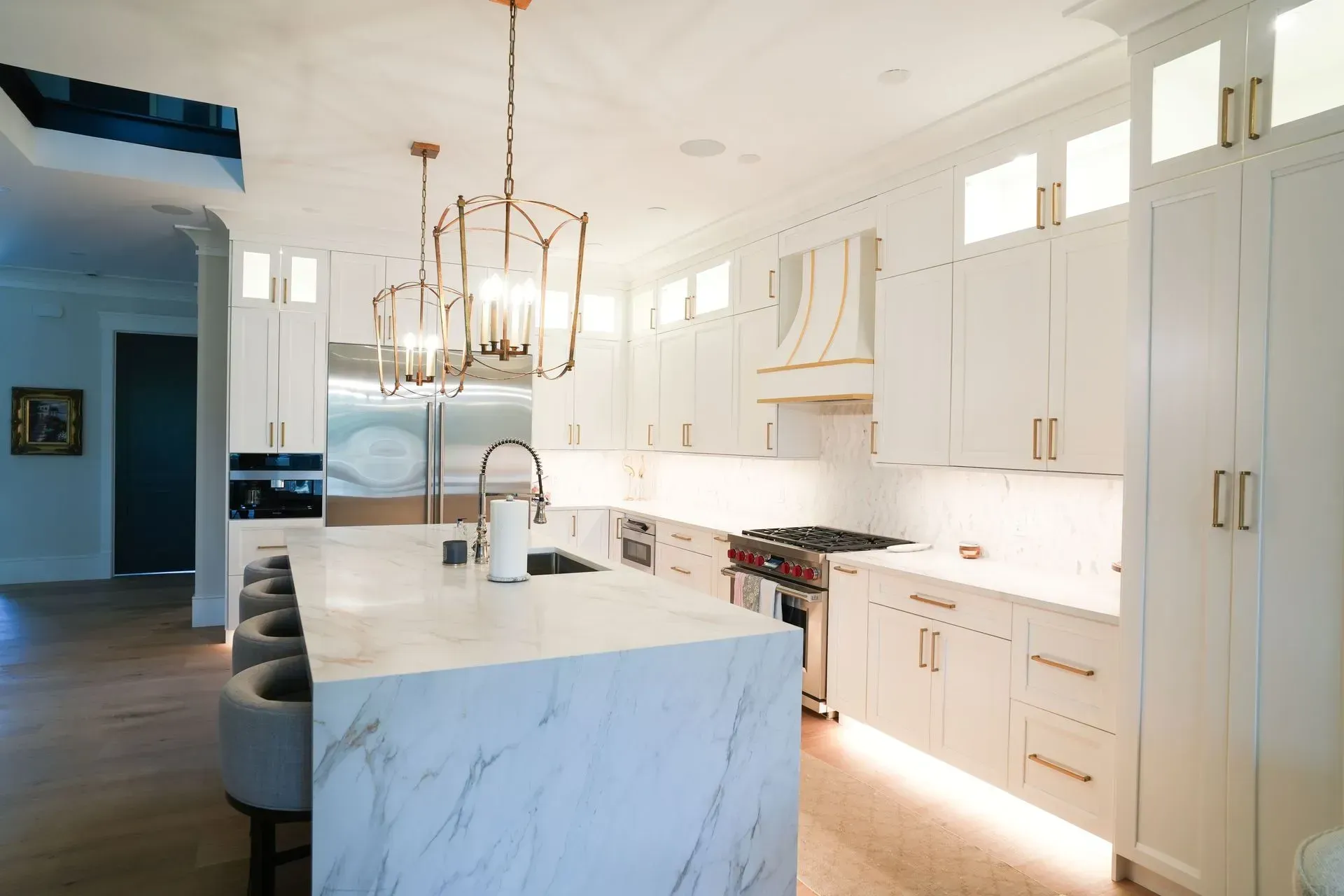 Luxurious white kitchen with marble island, gold accents, and pendant lights.