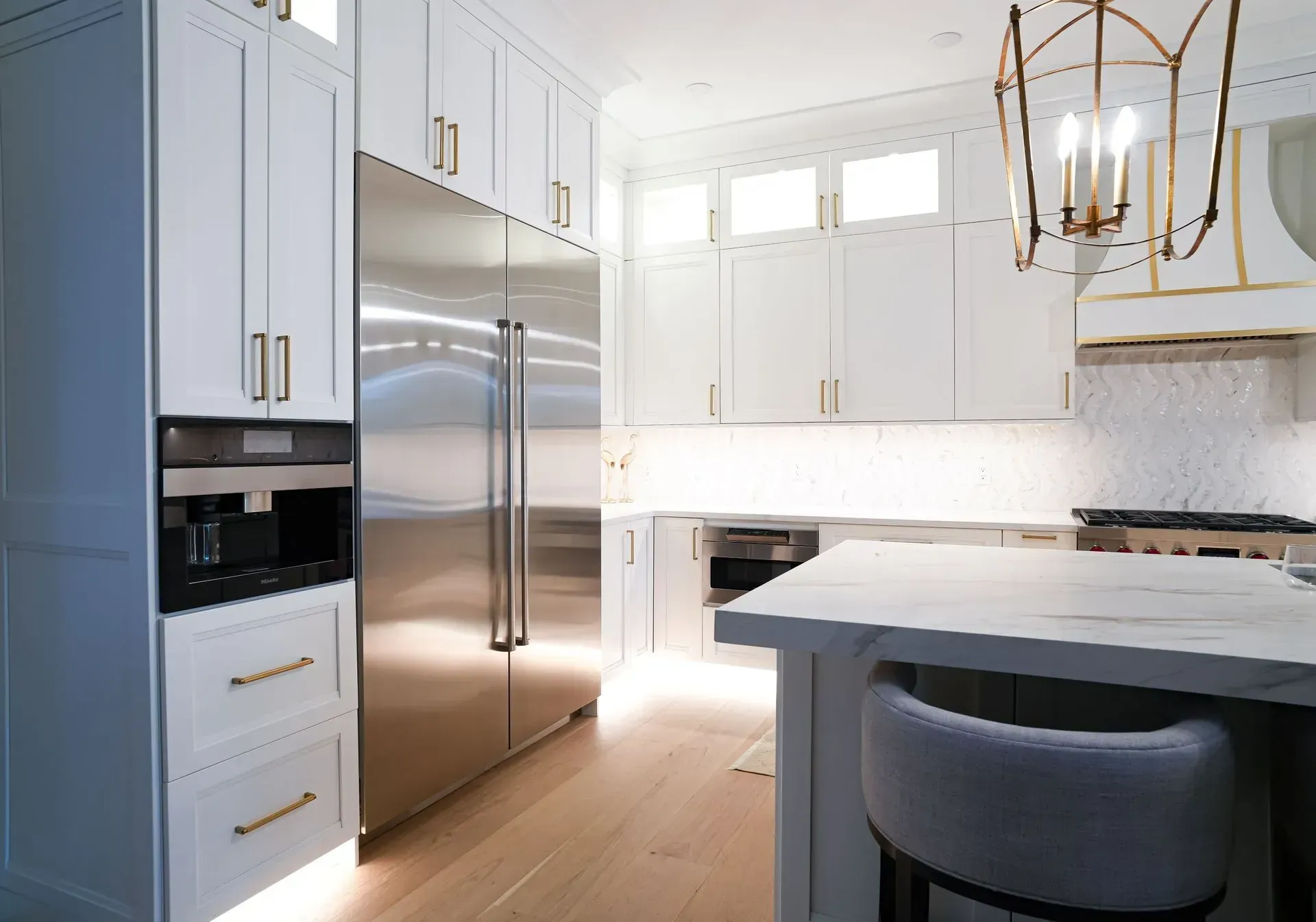 Modern white kitchen with stainless steel appliances, marble countertops, and gold accents.