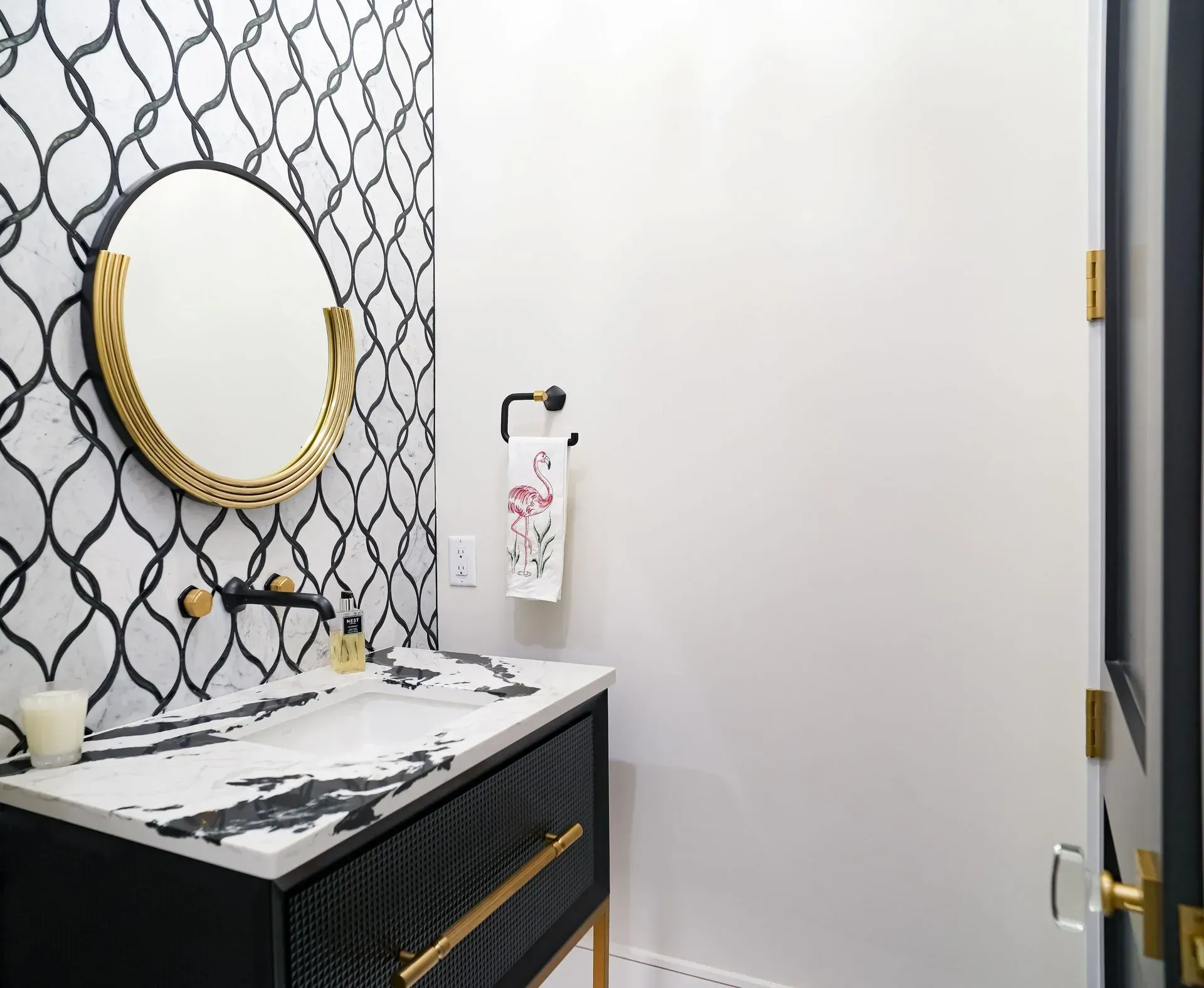 Bathroom with black and white patterned backsplash, black vanity, and gold accents.