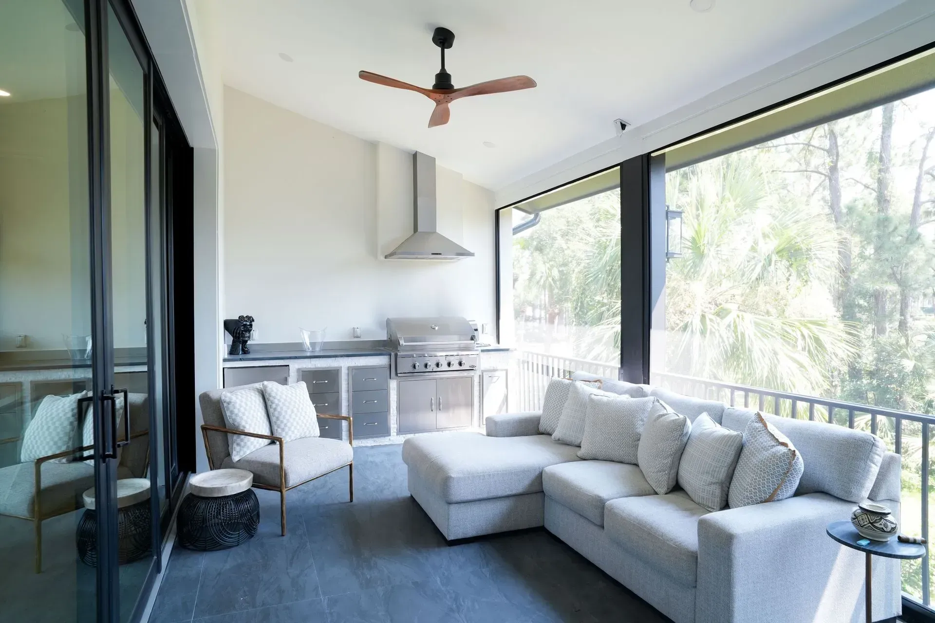 Outdoor kitchen and living space with a grill, sofa, and a fan.
