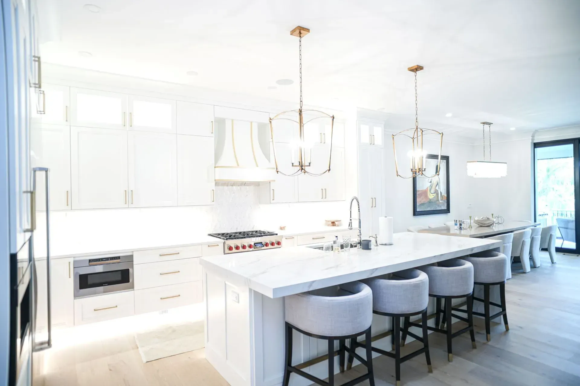 Bright, white kitchen with island seating and pendant lights. A dining table is visible in the background.