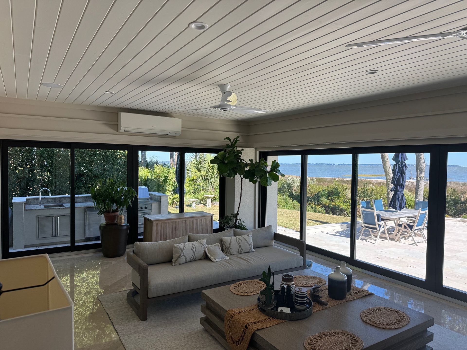 Sunroom with large windows, coastal view, gray couch, and light wood coffee table.