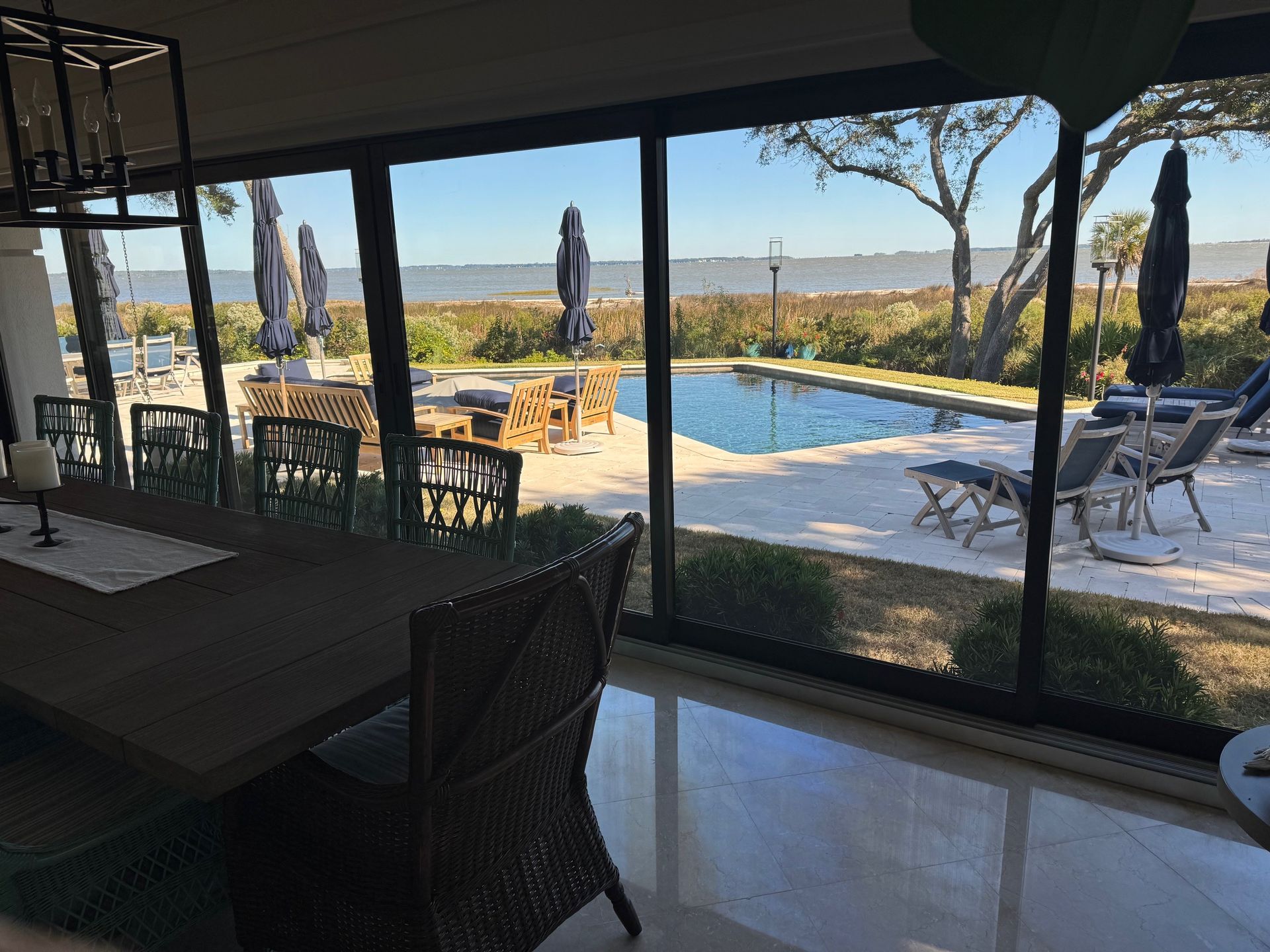 Outdoor dining area with a view of a pool, beach, and ocean through screened windows.