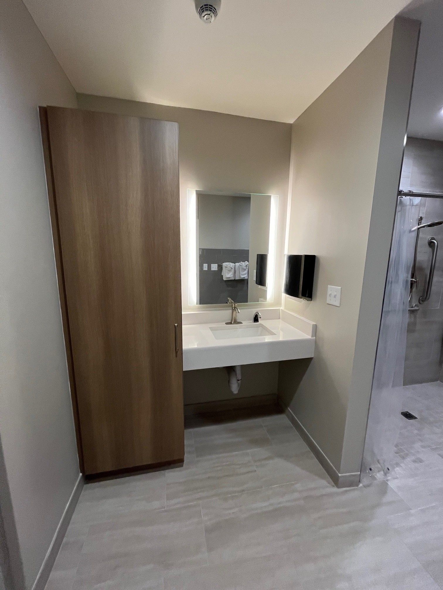 Bathroom with a sink, mirror, and cabinet. Shower visible on the right. Beige walls, light gray floor.