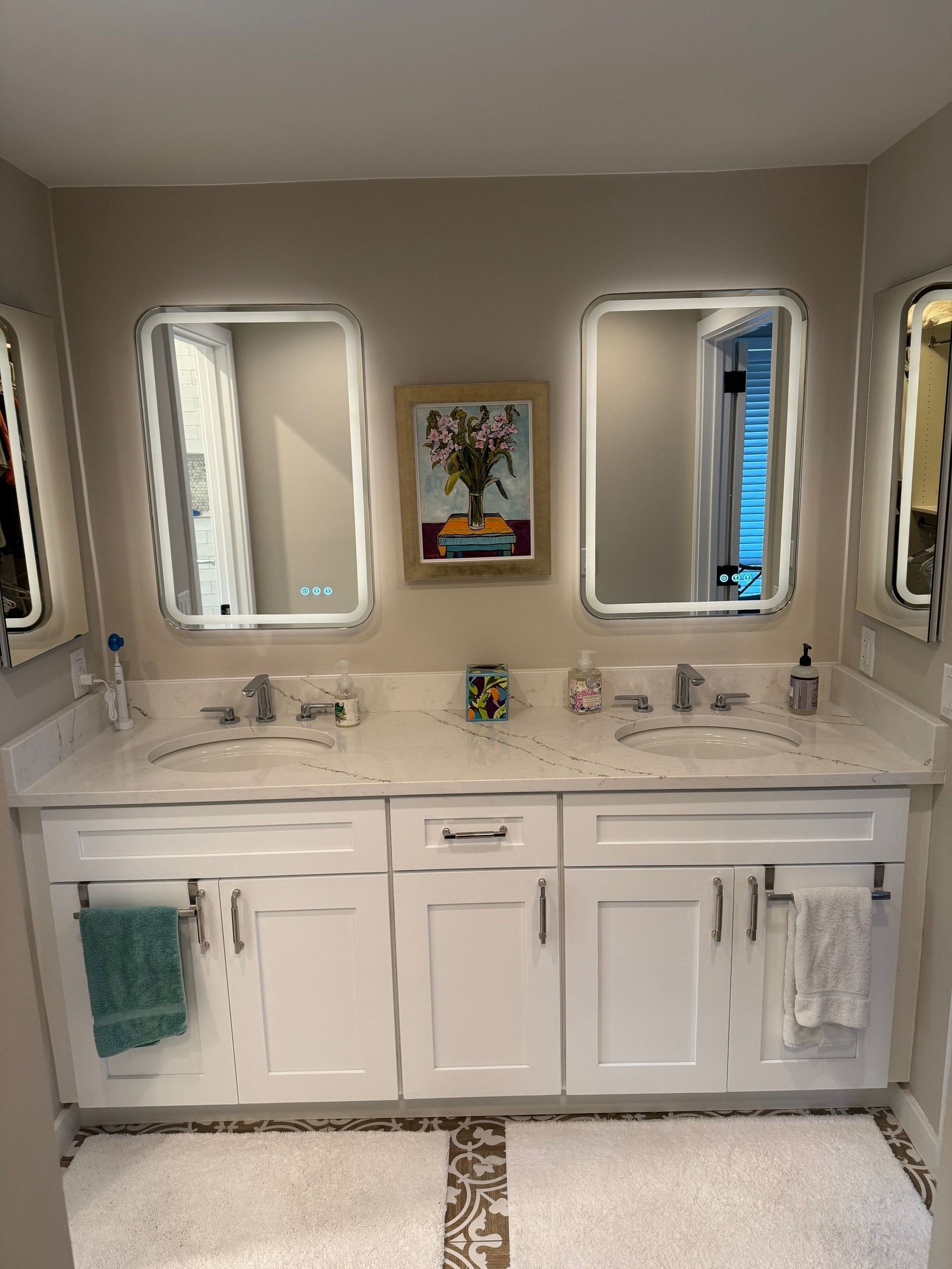 White bathroom vanity with three mirrors, artwork, and towels.