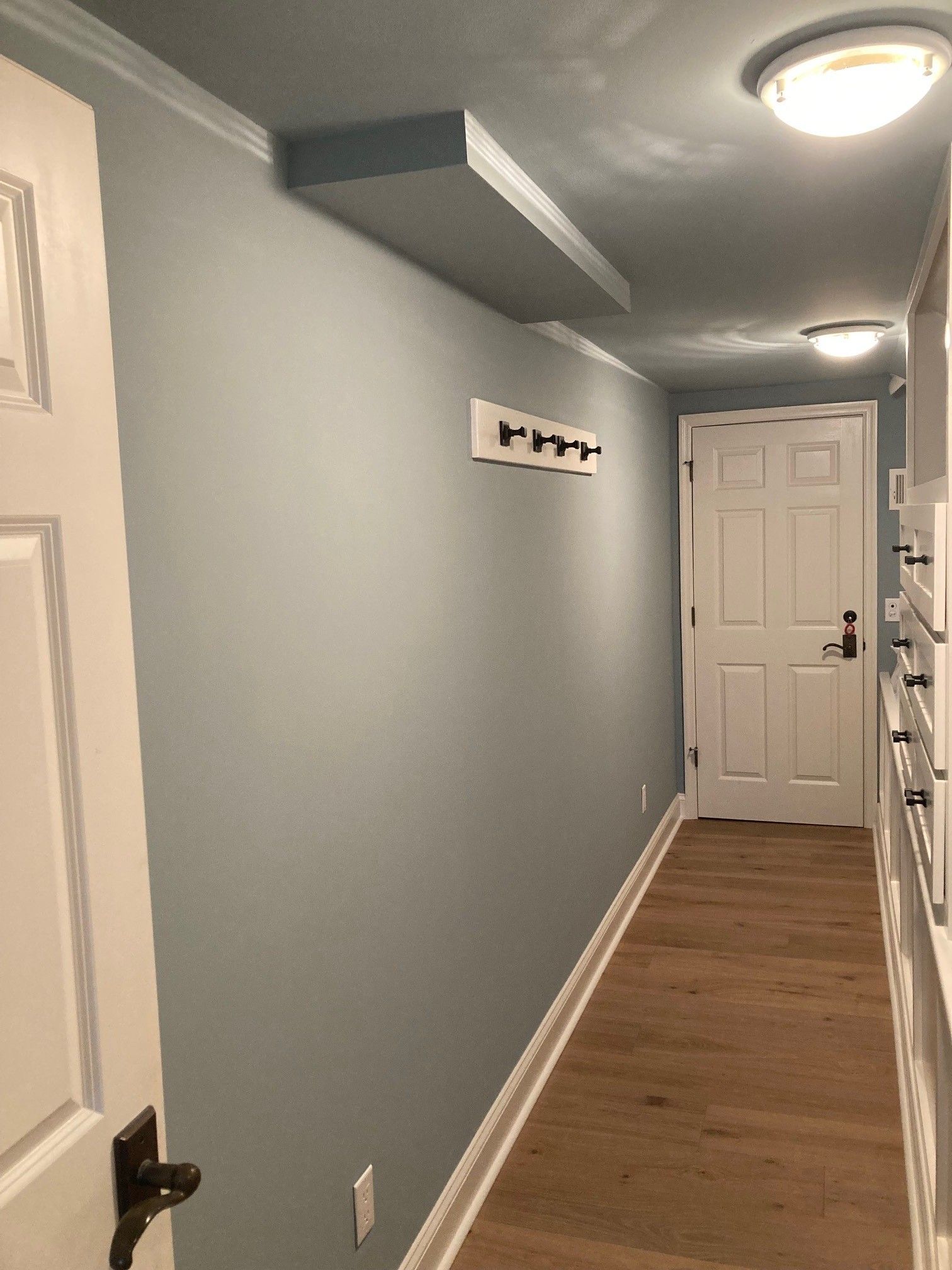 Hallway with light blue walls, wood floor, white doors, and coat hooks.