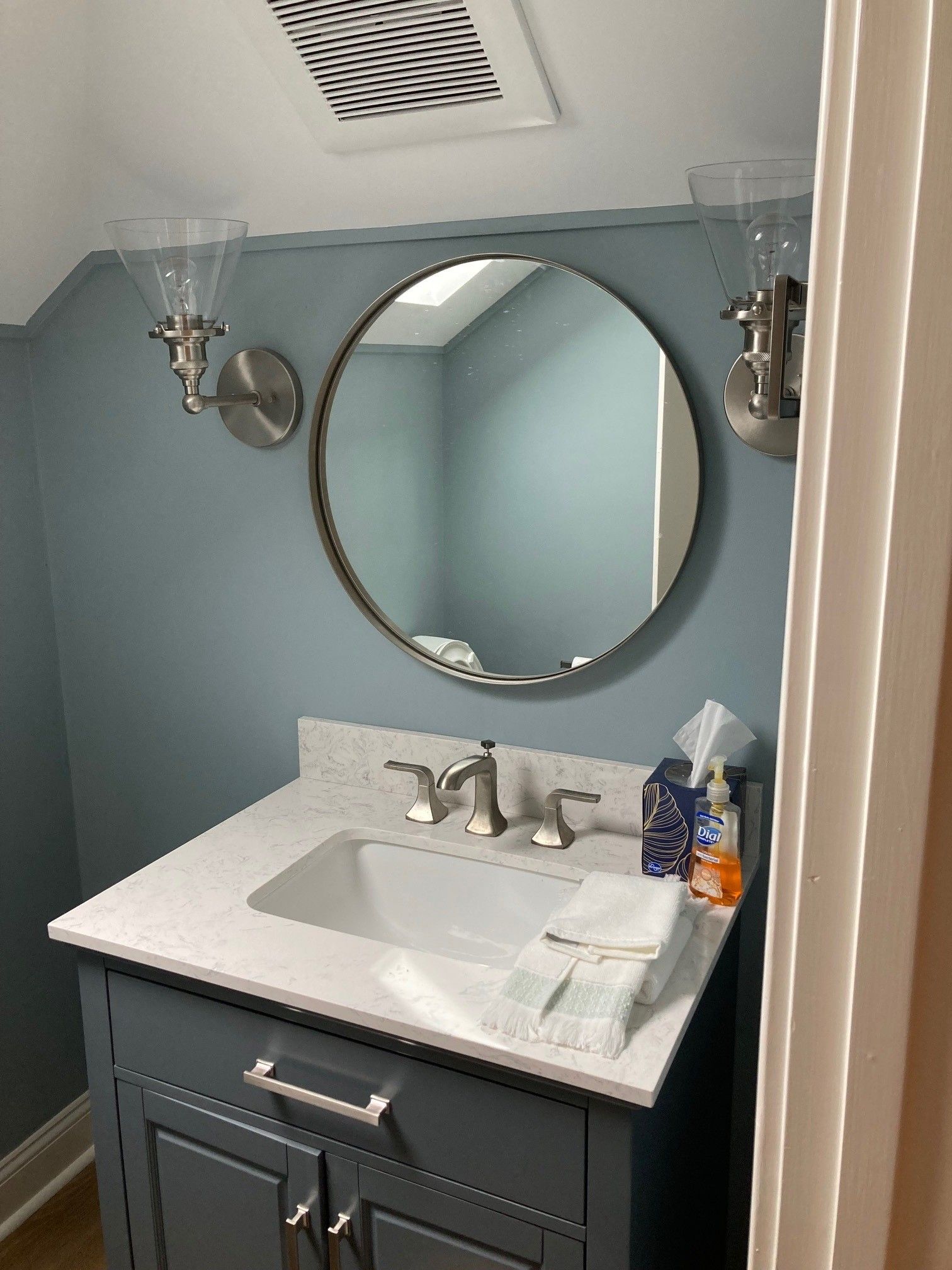 Bathroom vanity with round mirror, gray cabinet, blue wall, white countertop.