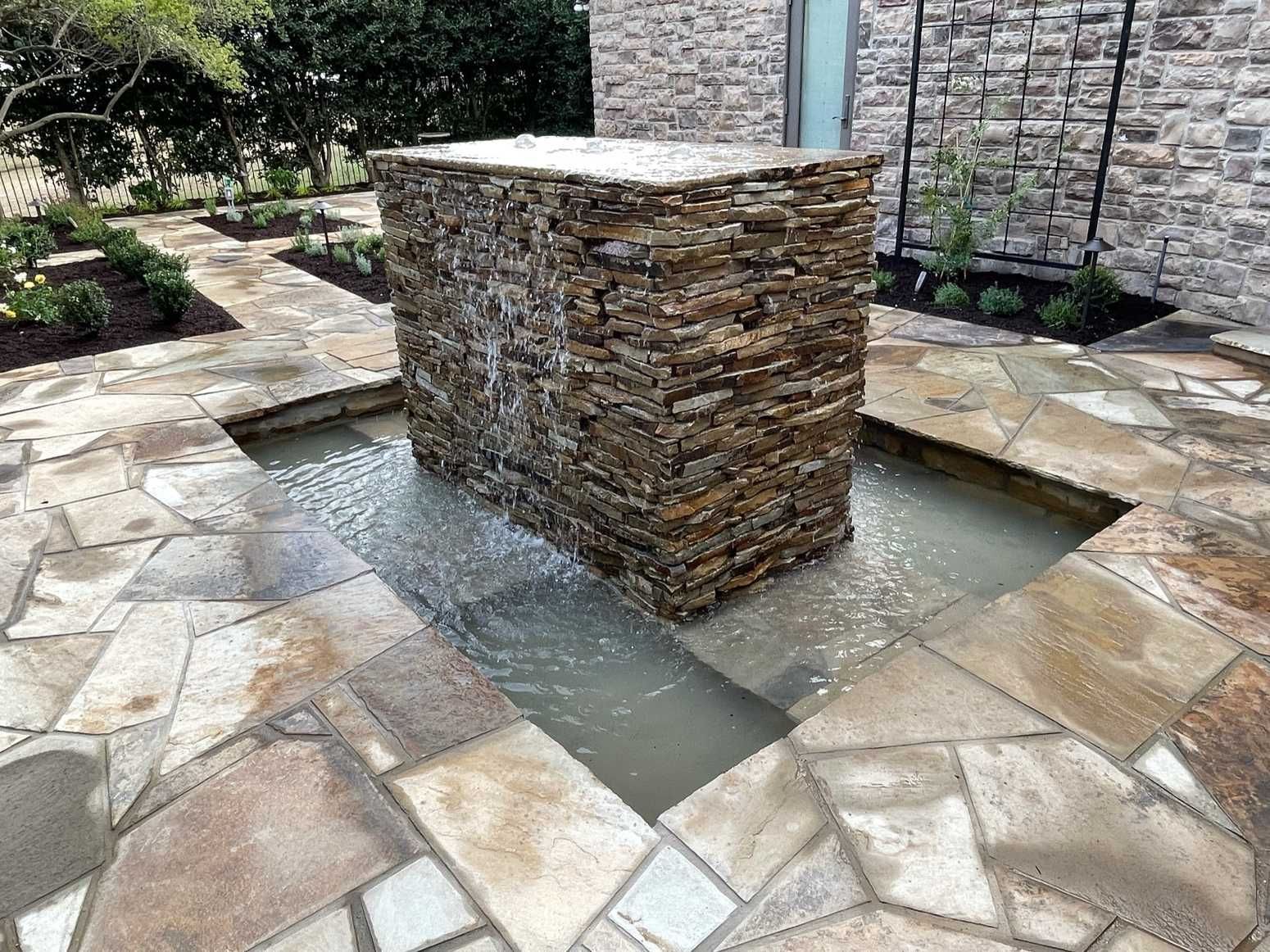 A stone fountain is in the middle of a stone patio.
